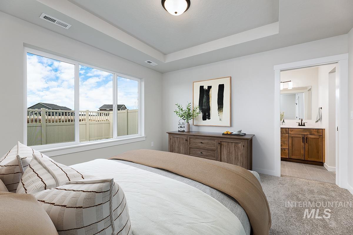 Bedroom with a tray ceiling, light carpet, and connected bathroom