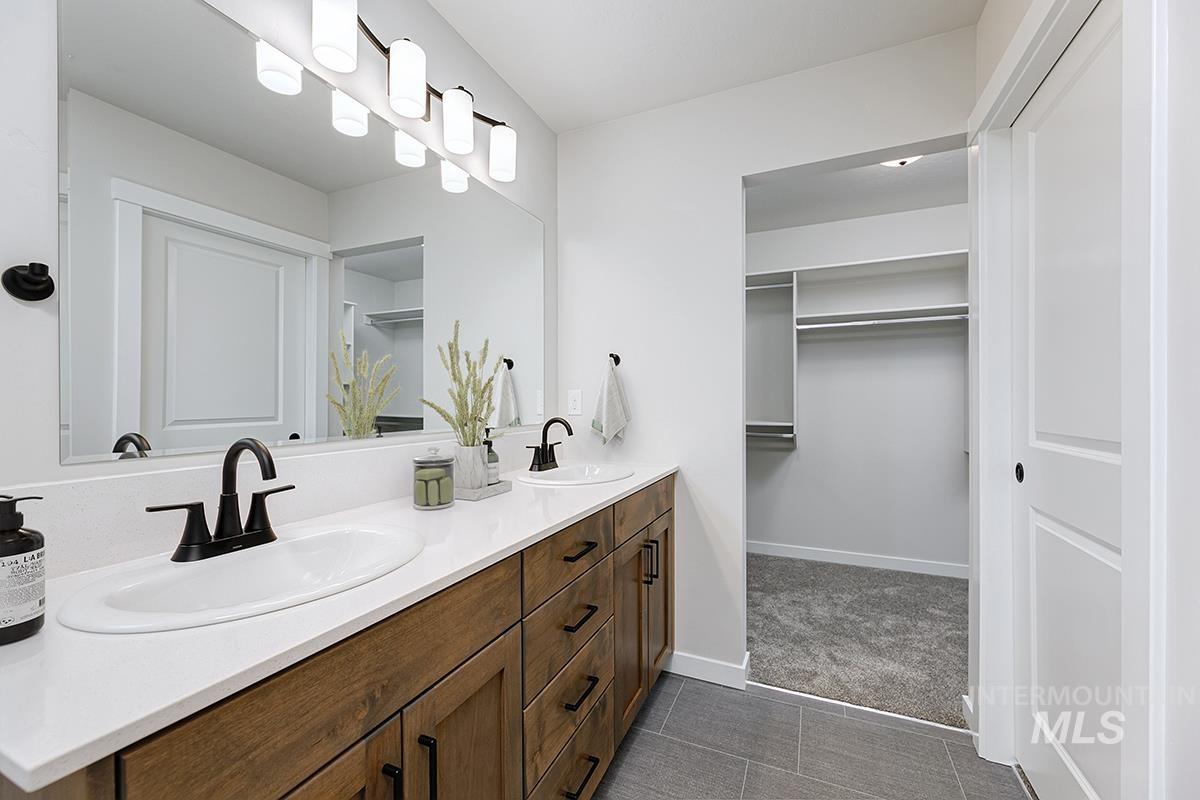 Bathroom featuring double vanity, dark colored carpet, a walk in closet, and dark tile patterned floors