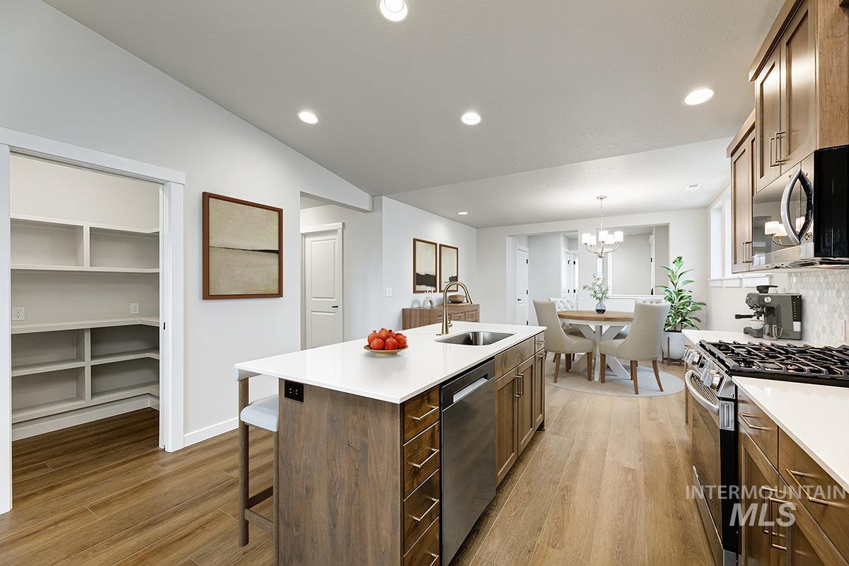 Kitchen featuring appliances with stainless steel finishes, light wood-style floors, brown cabinetry, a center island with sink, and recessed lighting
