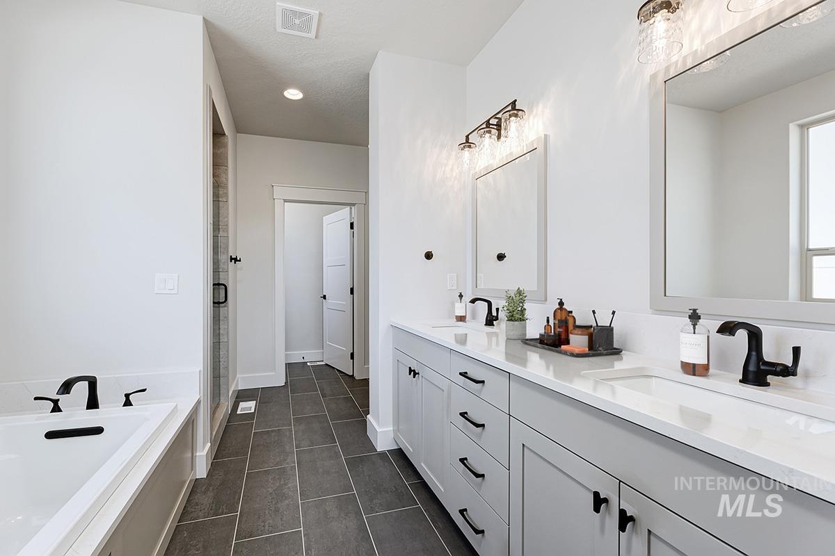 Bathroom featuring double vanity, a garden tub, dark tile patterned floors, and a stall shower