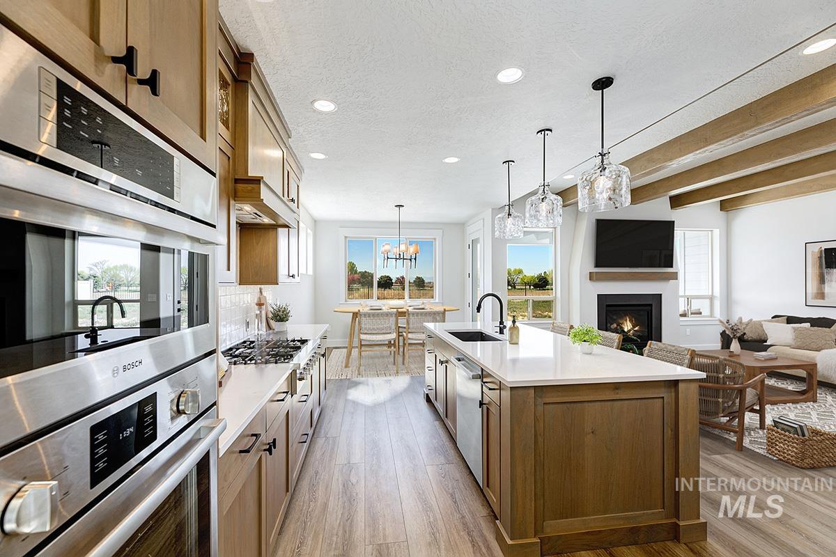 Kitchen featuring brown cabinetry, stainless steel appliances, a warm lit fireplace, hanging light fixtures, and recessed lighting
