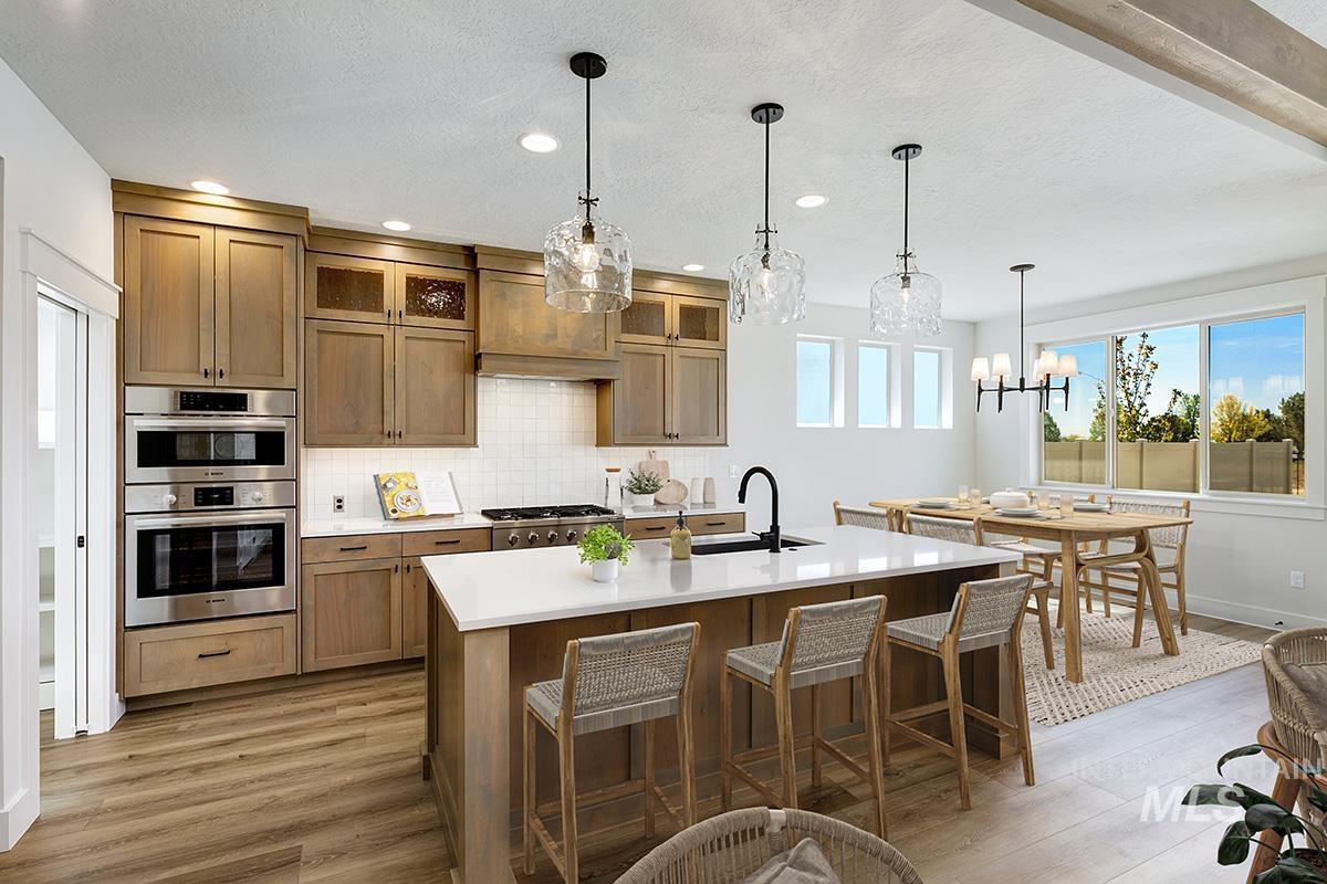 Kitchen with pendant lighting, brown cabinets, custom exhaust hood, decorative backsplash, and an island with sink