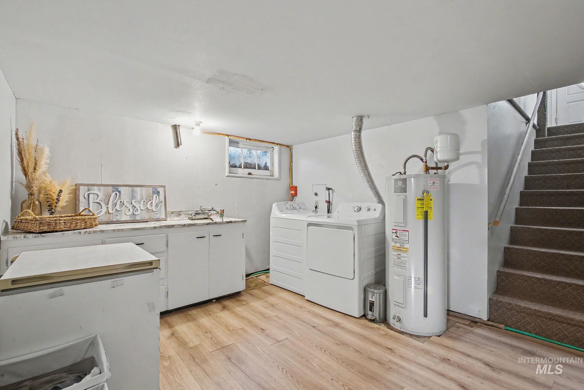 Laundry room with water heater, light wood-style floors, cabinet space, and separate washer and dryer