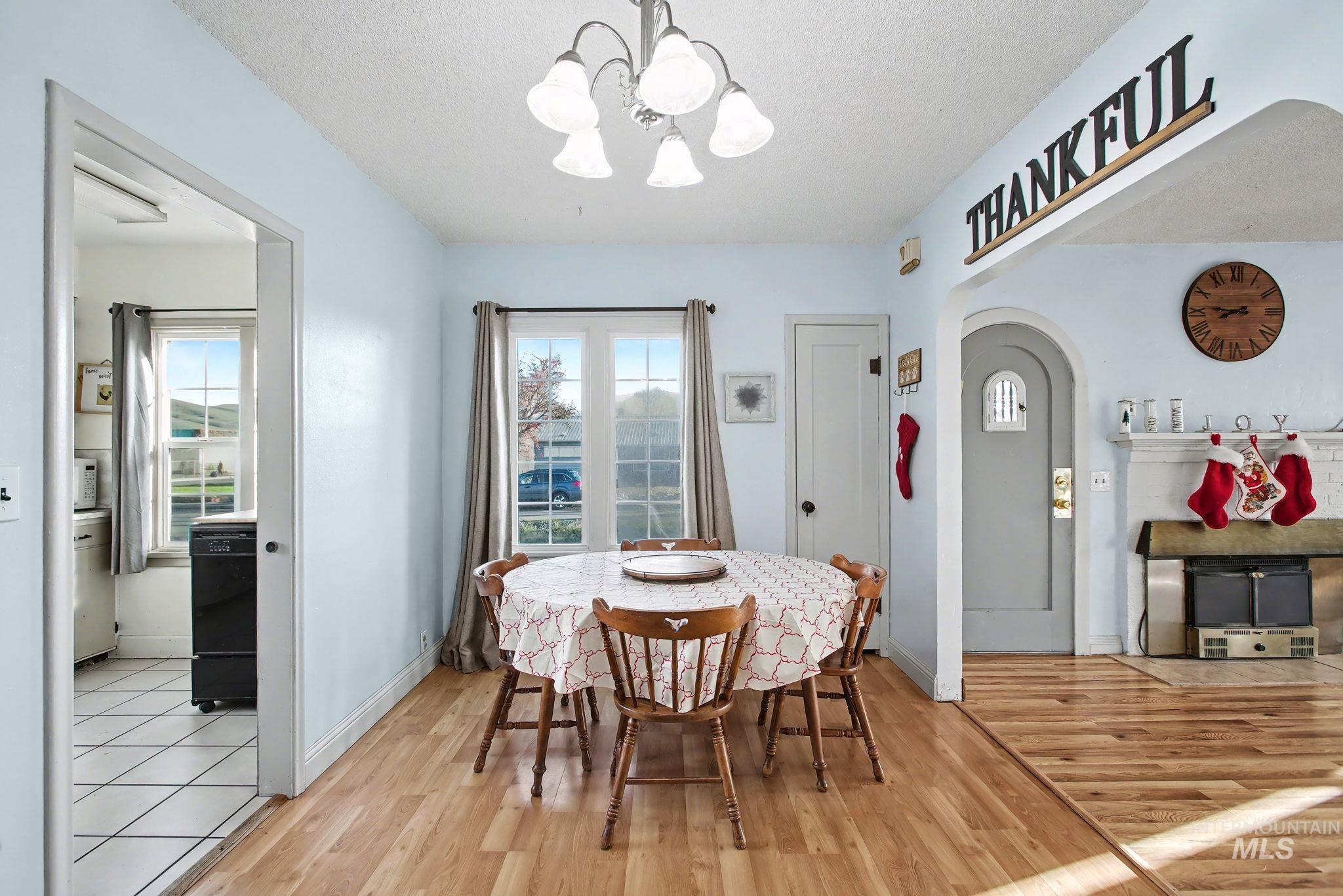Dining area featuring healthy amount of natural light, a textured ceiling, light wood-style floors, arched walkways, and a chandelier
