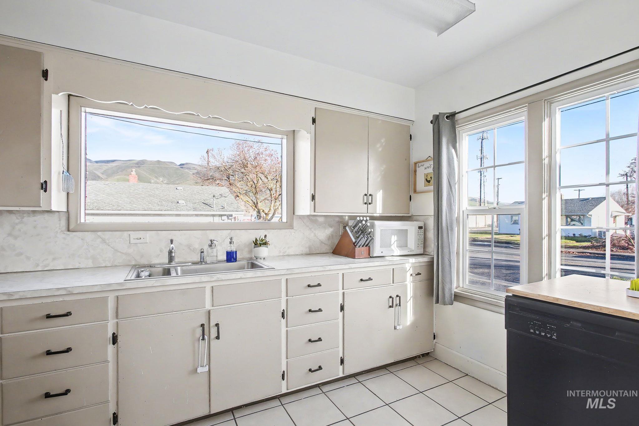 Kitchen with black dishwasher, light countertops, white microwave, and light tile patterned flooring
