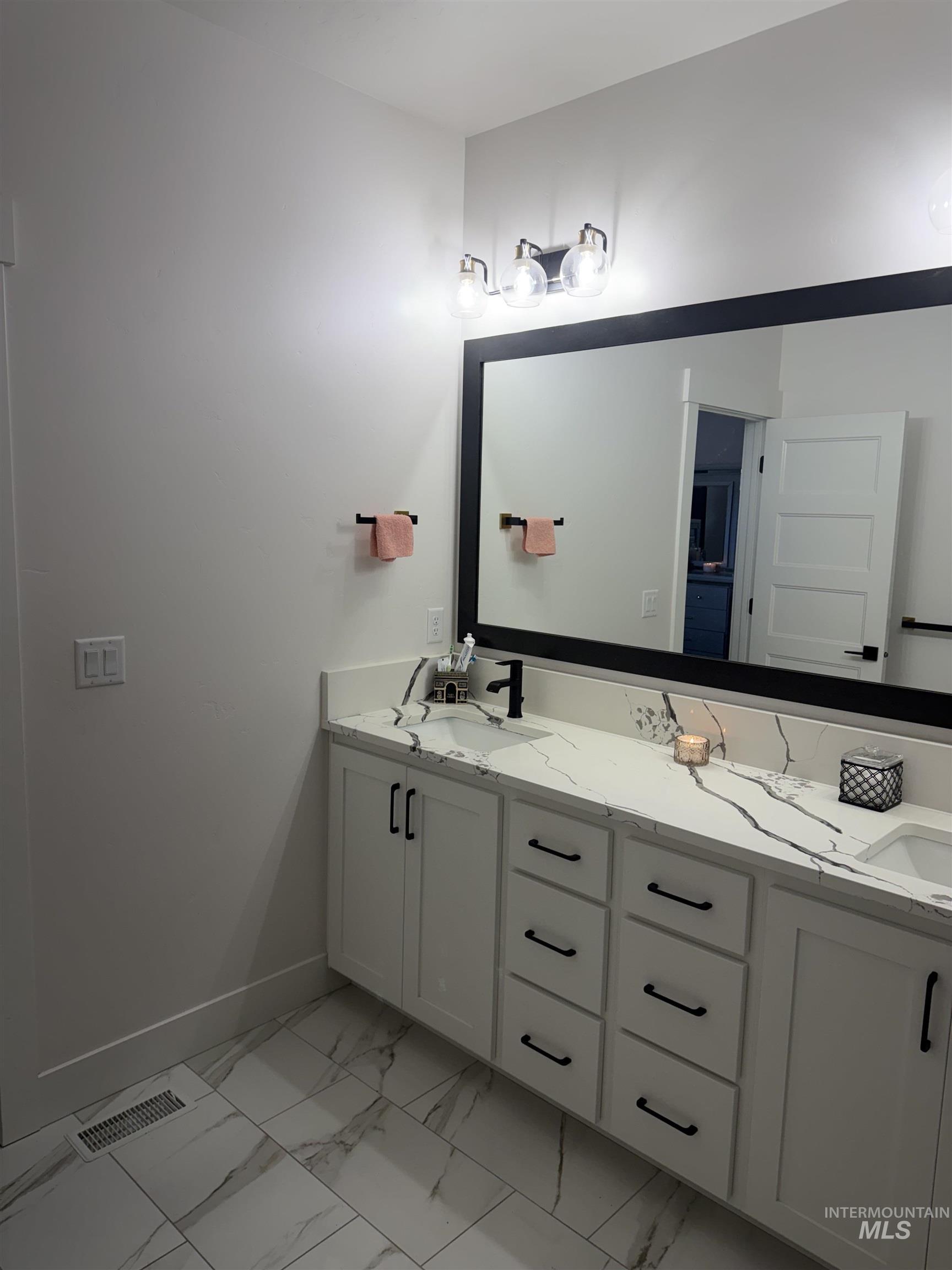 Full bath featuring double vanity and light marble finish floors