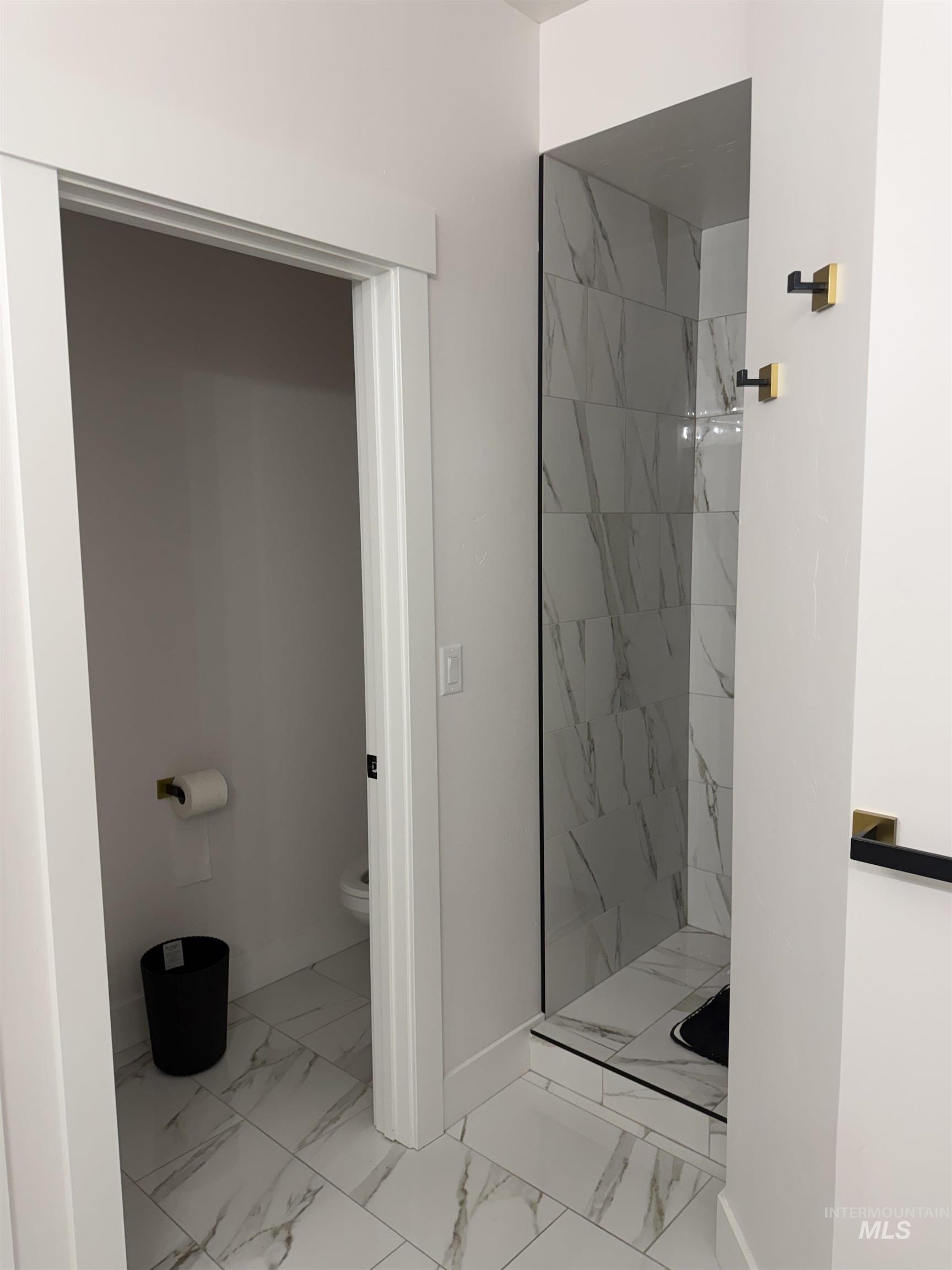 Full bath featuring light marble finish floors and a marble finish shower