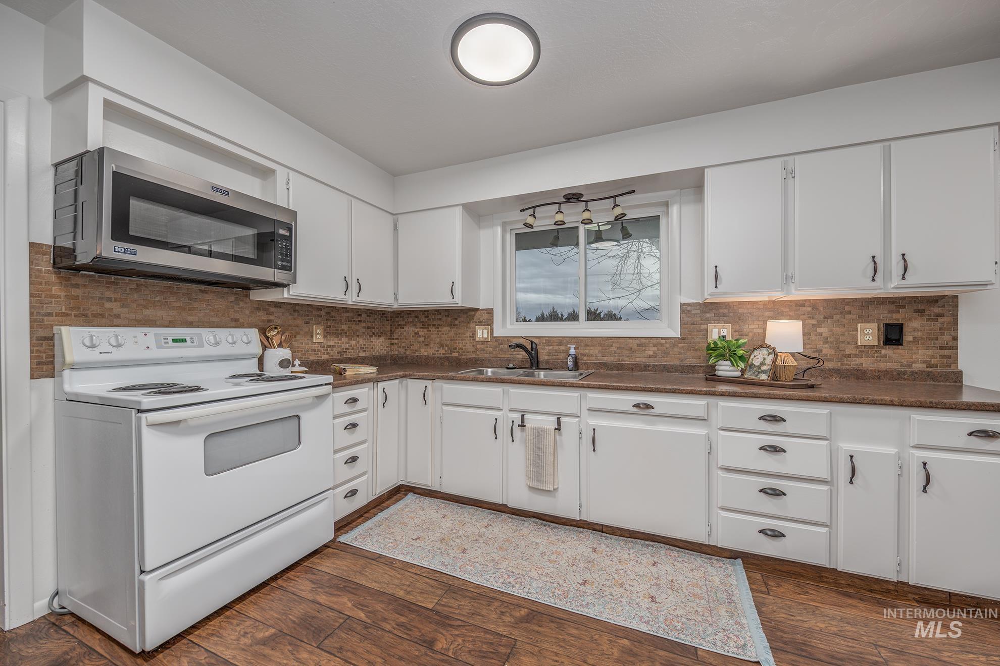 Kitchen featuring white electric range, stainless steel microwave, and white cabinetry