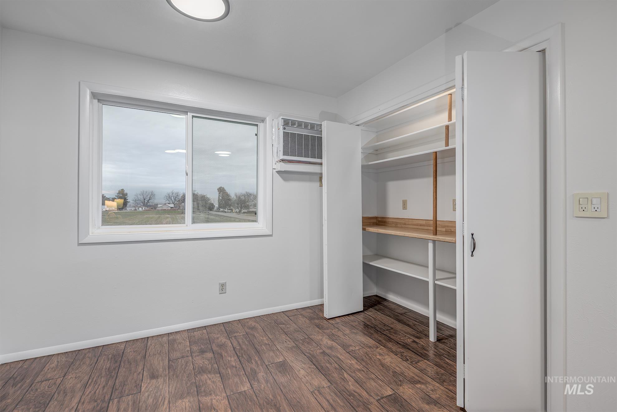 Unfurnished kitchen nook featuring dark wood finished floors, a wall mounted AC, and a pantry