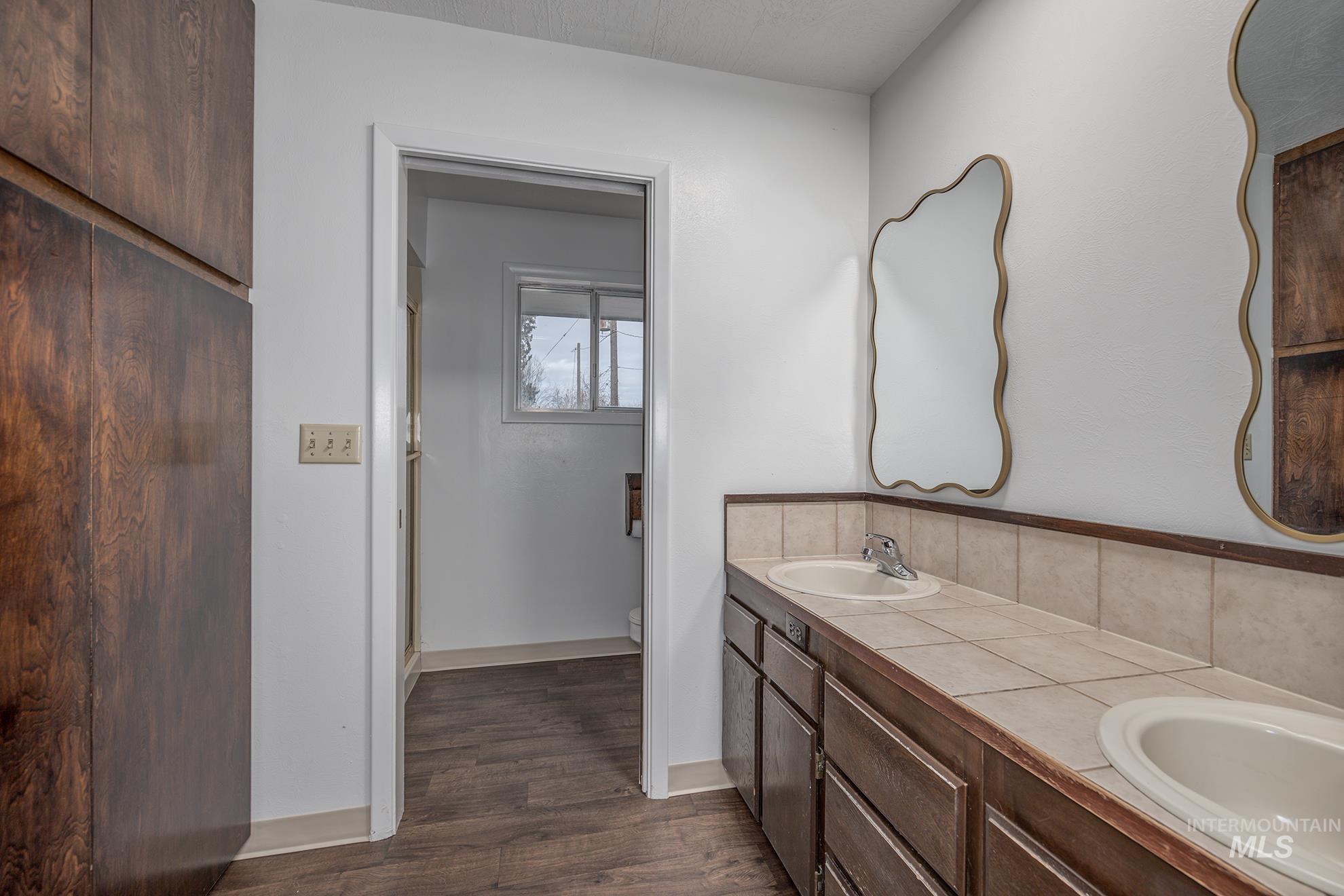 Full bath featuring a shower stall, double vanity, and dark wood-type flooring