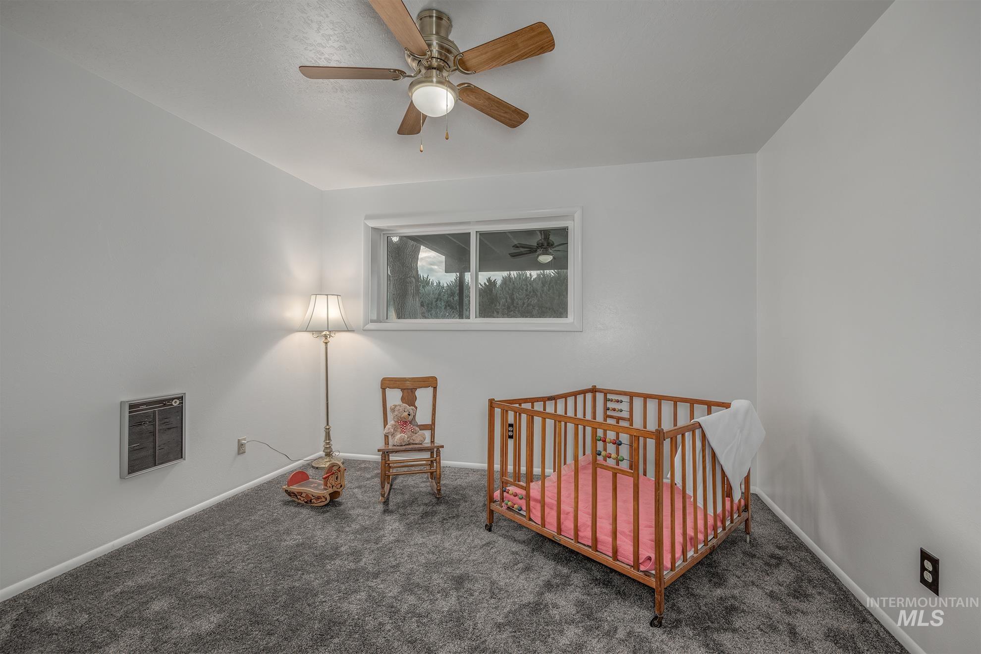 Carpeted bedroom with a crib, heating unit, and ceiling fan