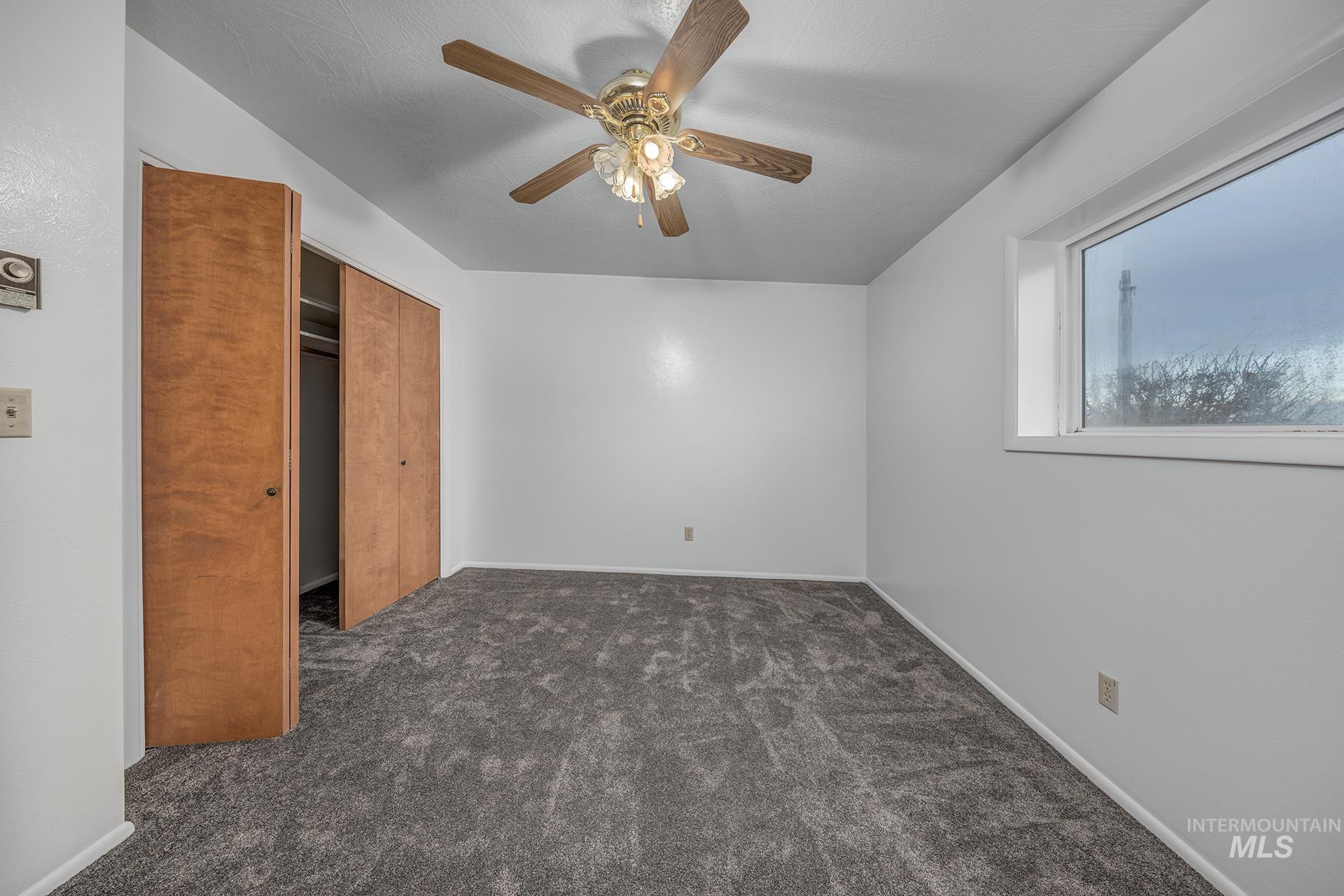 Unfurnished bedroom featuring dark colored carpet, ceiling fan, and a closet