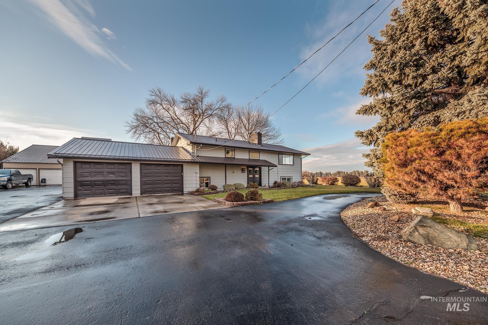 View of front of house featuring driveway, a chimney, an attached garage, a metal roof, and covered porch