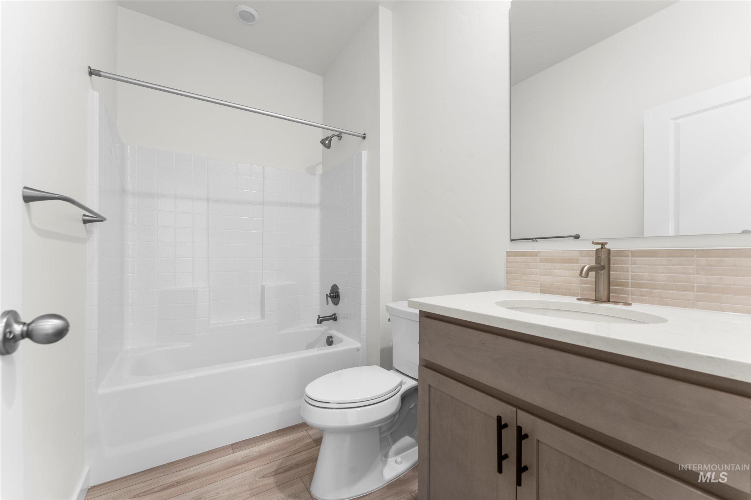 Bathroom featuring light wood-style flooring, vanity, washtub / shower combination, and tasteful backsplash