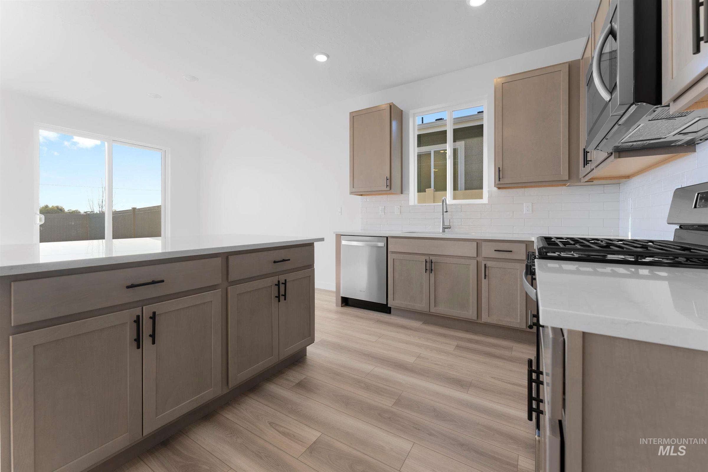 Kitchen featuring appliances with stainless steel finishes, tasteful backsplash, light stone counters, light wood-style flooring, and recessed lighting