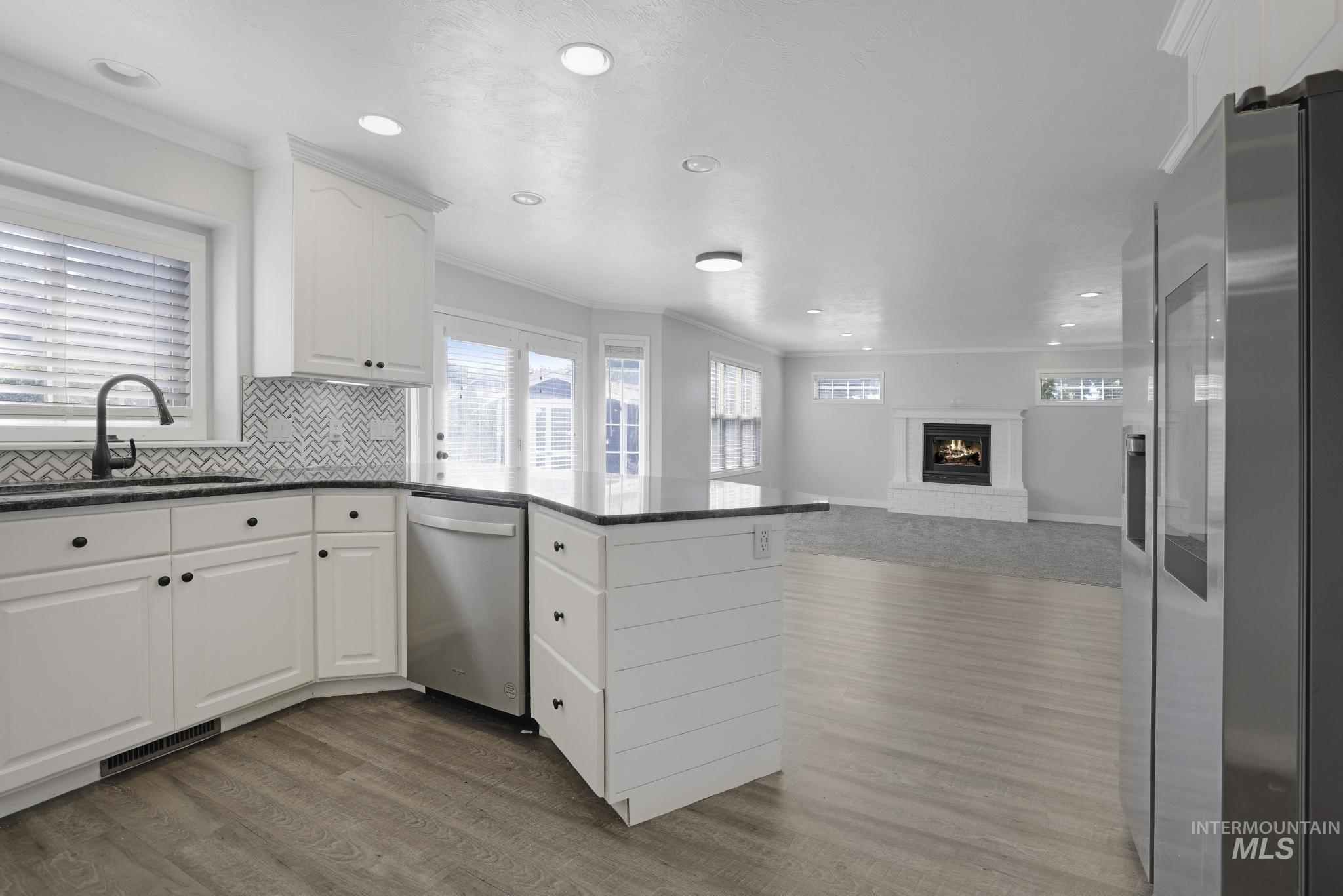 Kitchen with ornamental molding, stainless steel appliances, white cabinets, dark stone countertops, and a peninsula