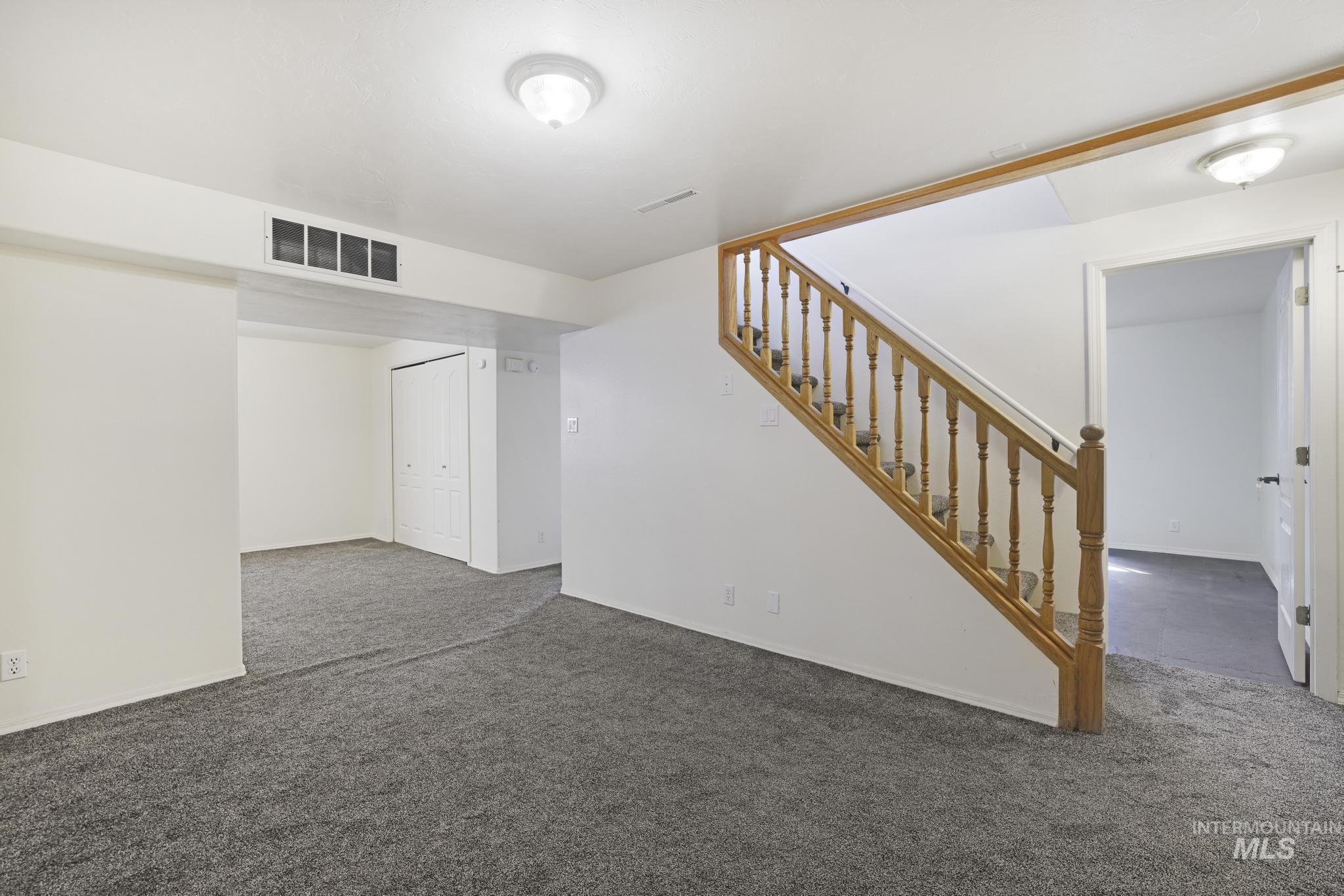 Unfurnished living room featuring carpet flooring and stairway