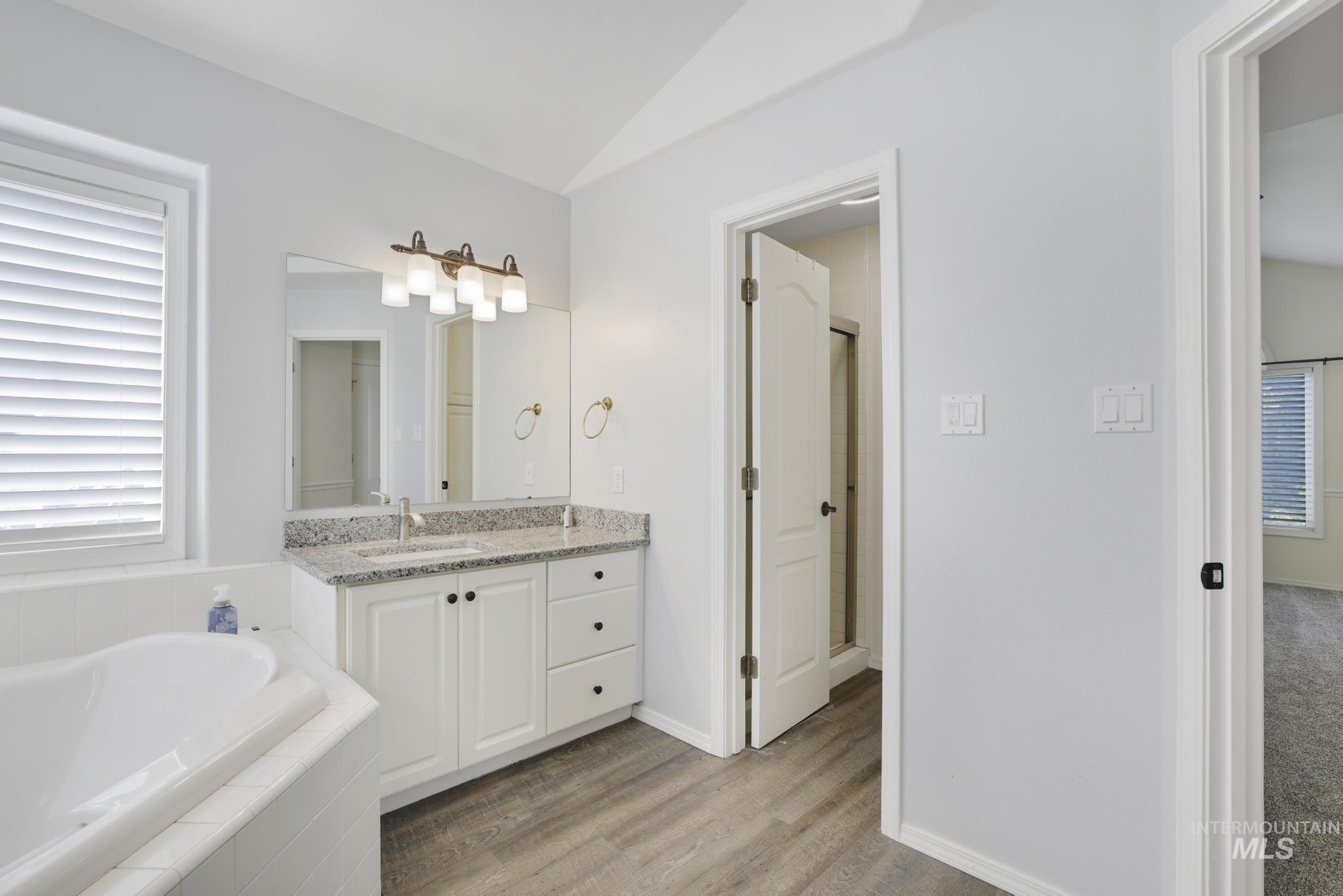 Bathroom featuring vanity, a bath, light wood-style flooring, and lofted ceiling
