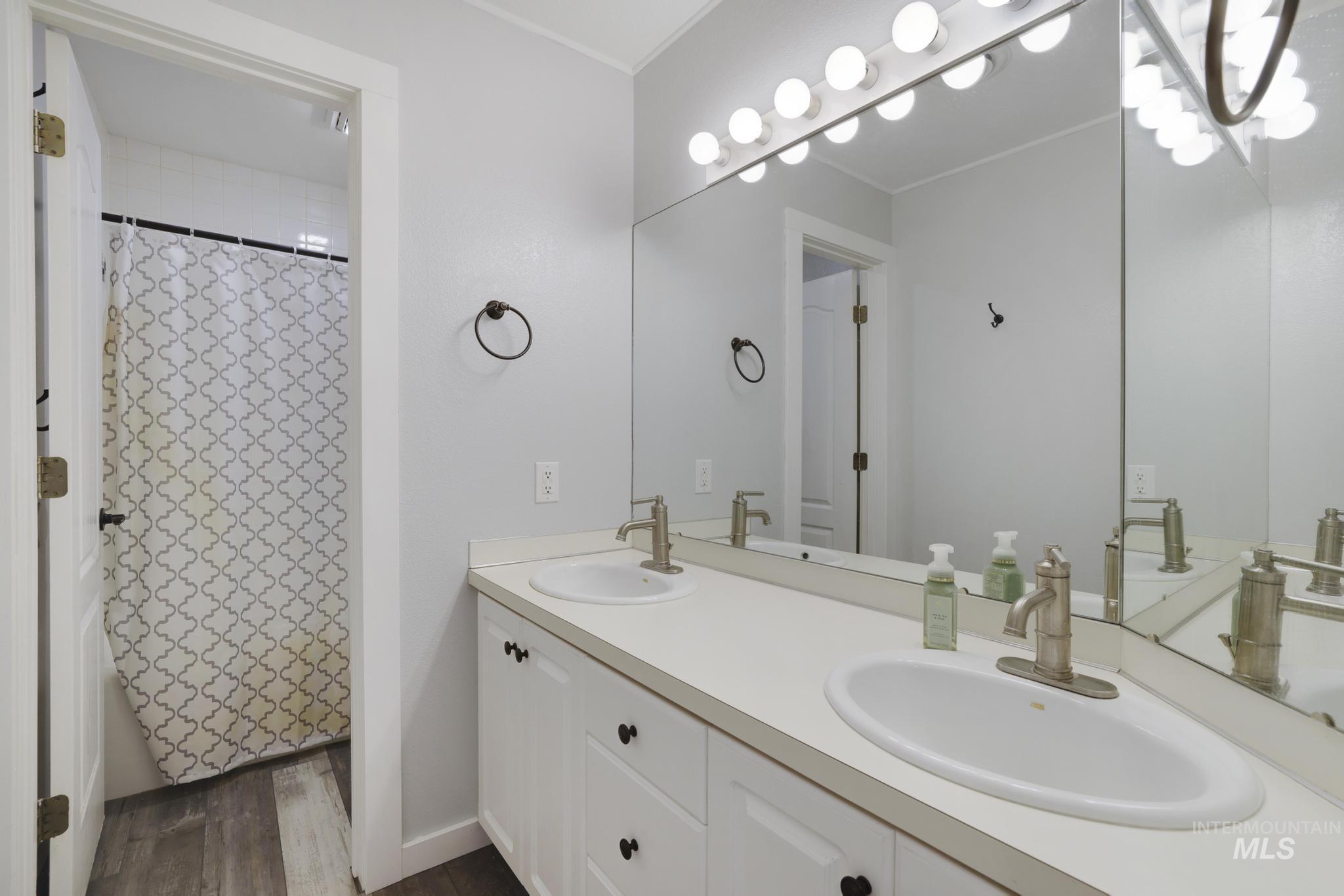 Bathroom with double vanity, dark wood-style flooring, and shower / bathtub combination with curtain
