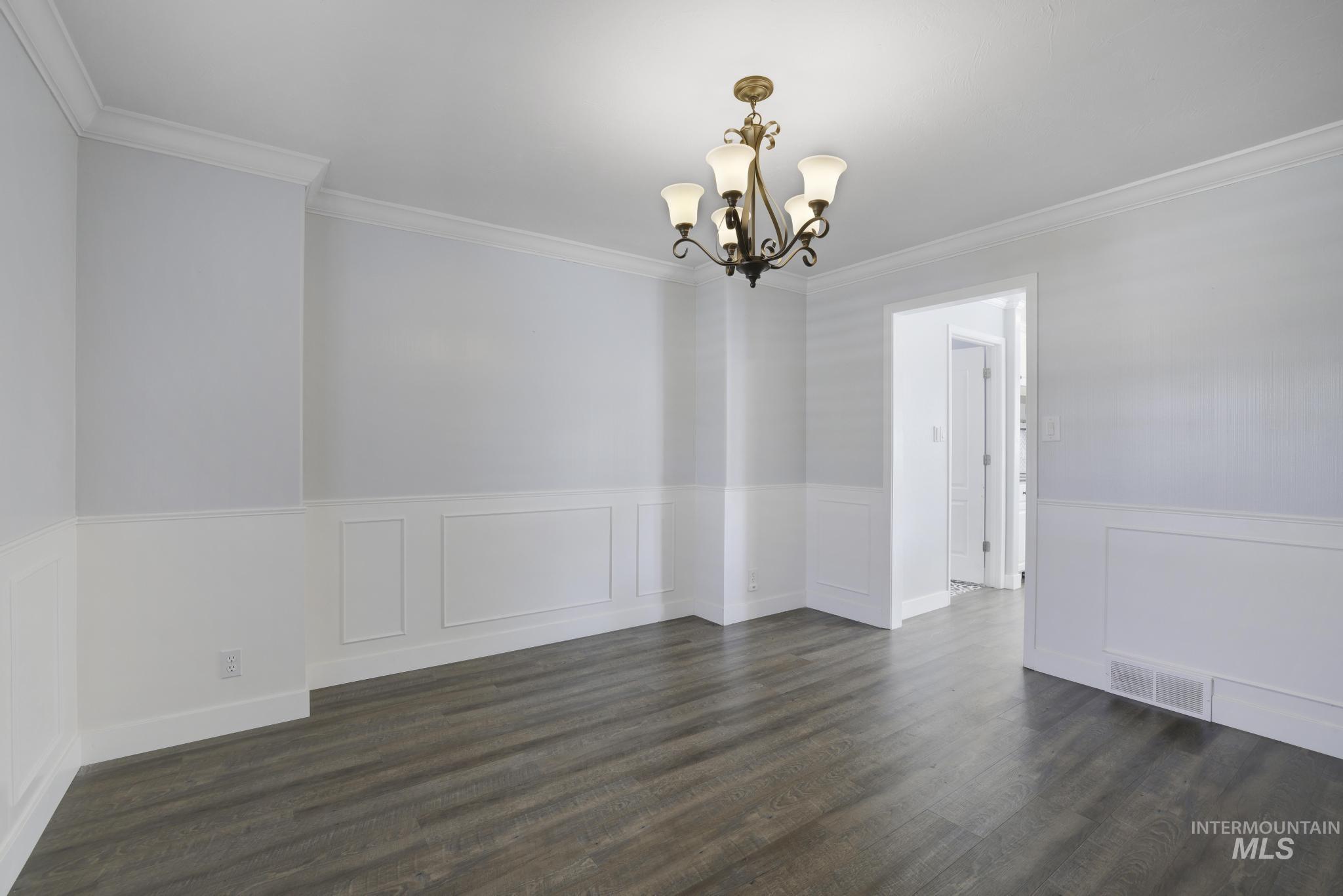 Unfurnished dining area featuring dark wood-style flooring, wainscoting, ornamental molding, a chandelier, and a decorative wall
