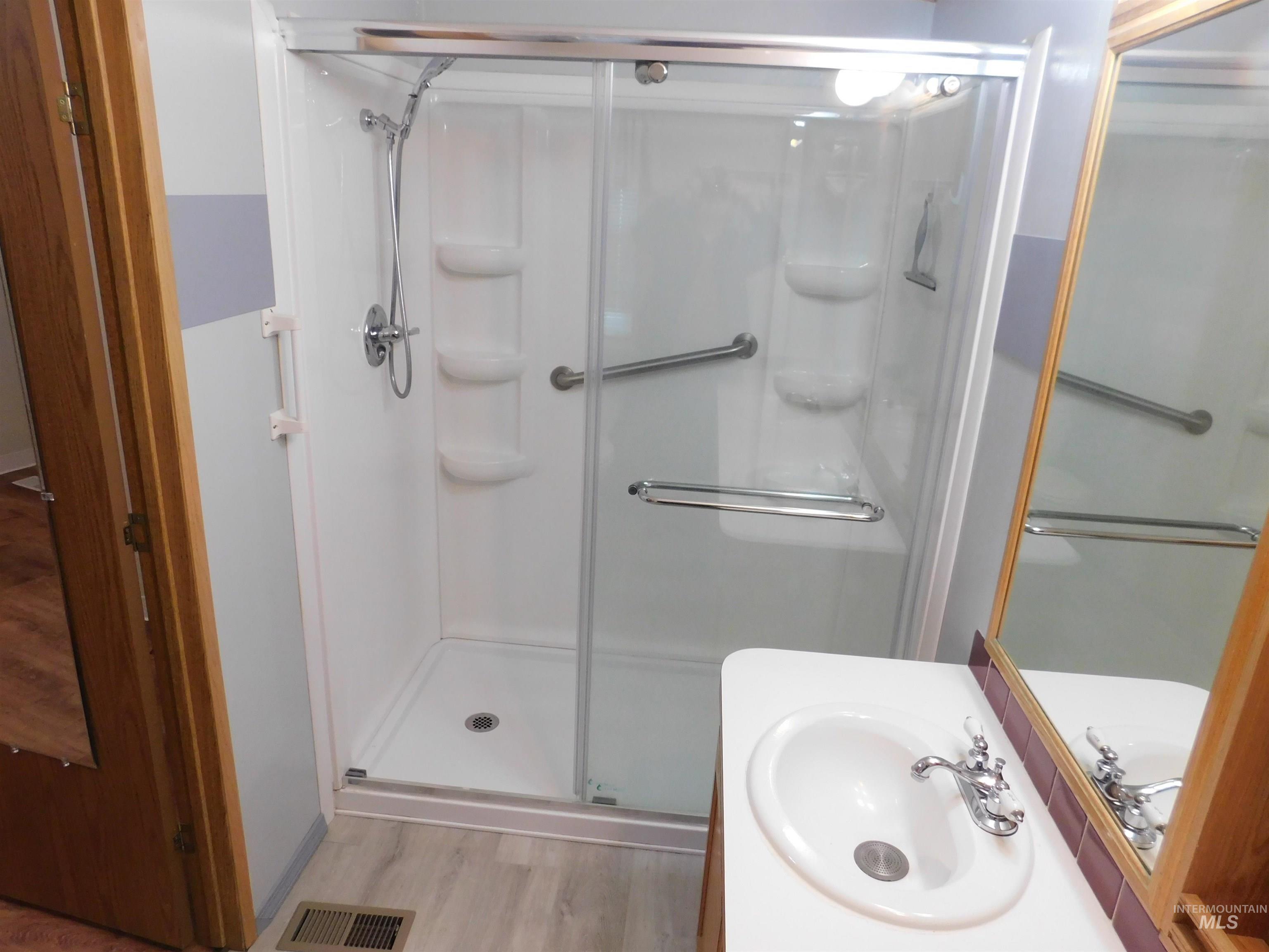Bathroom with light wood-style flooring, vanity, and a shower stall
