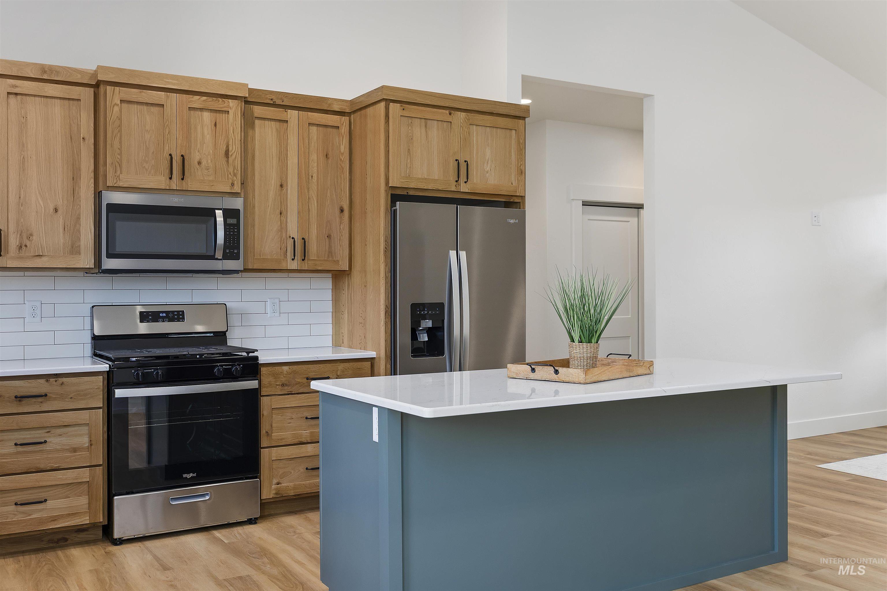 Kitchen featuring stainless steel appliances, backsplash, a center island, light wood-style floors, and light stone counters