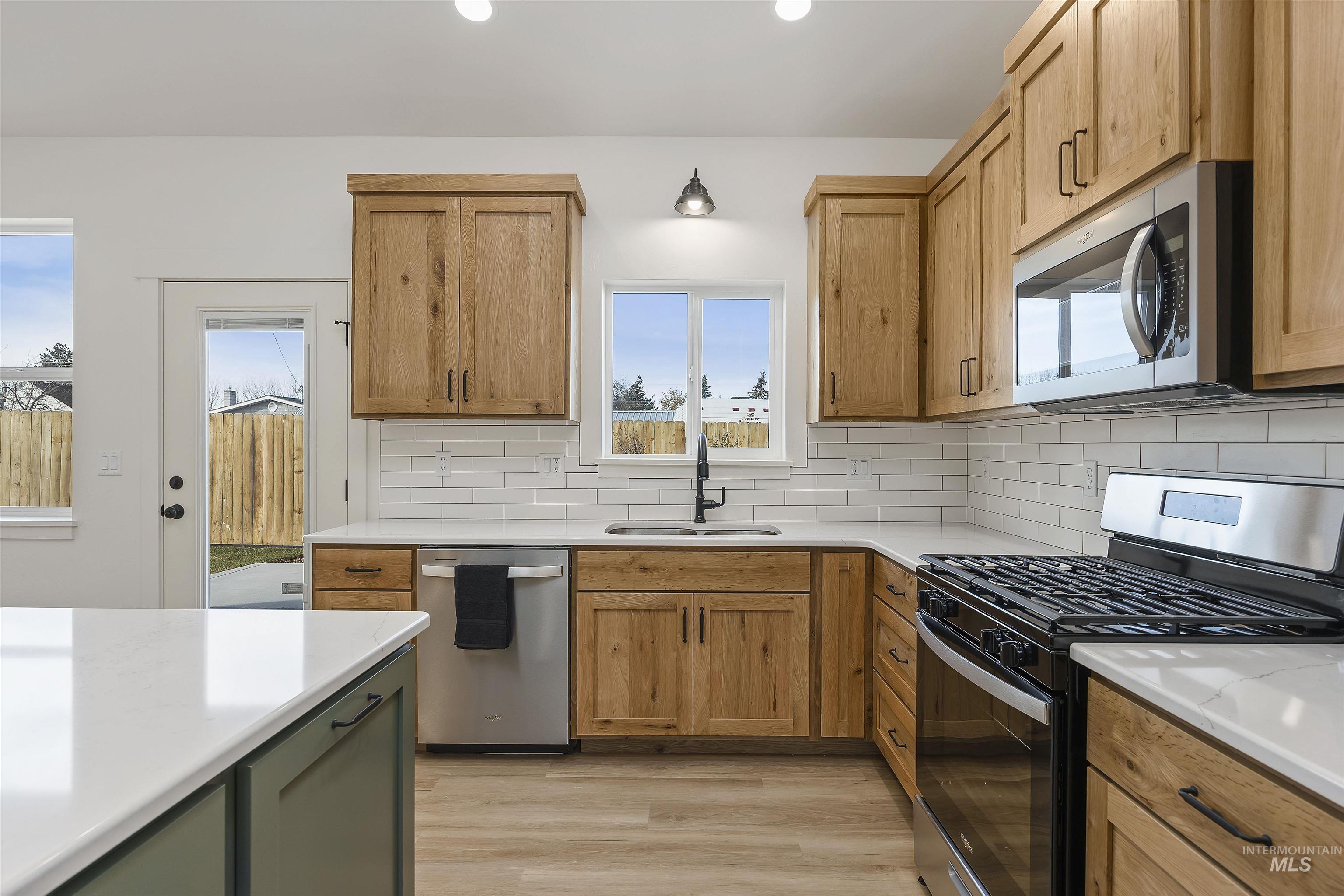 Kitchen with stainless steel appliances, backsplash, light wood-type flooring, light stone countertops, and recessed lighting
