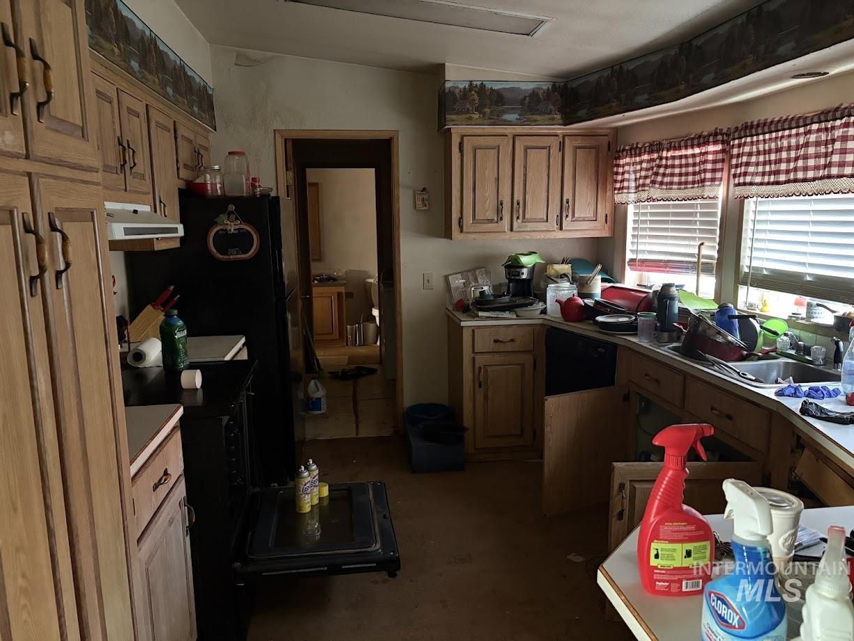 Kitchen featuring brown cabinets, under cabinet range hood, black appliances, and light countertops