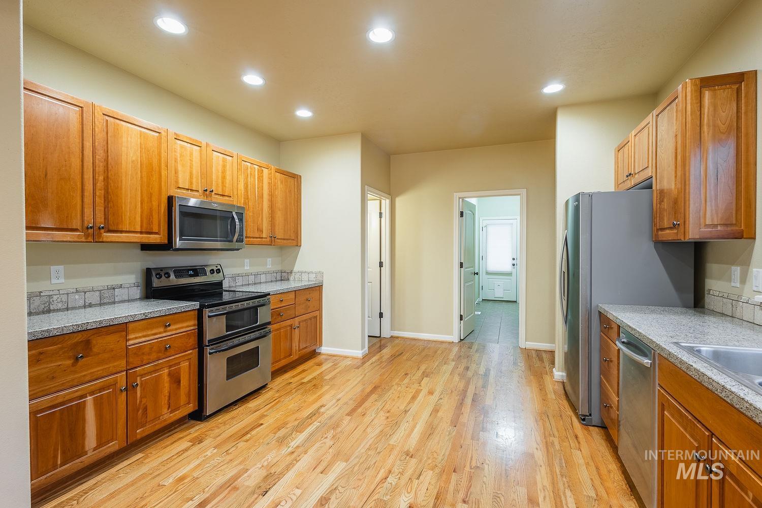Kitchen with appliances with stainless steel finishes, brown cabinetry, recessed lighting, light wood-style floors, and light stone counters