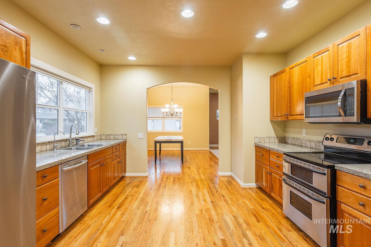 Kitchen with stainless steel appliances, arched walkways, recessed lighting, brown cabinets, and a chandelier