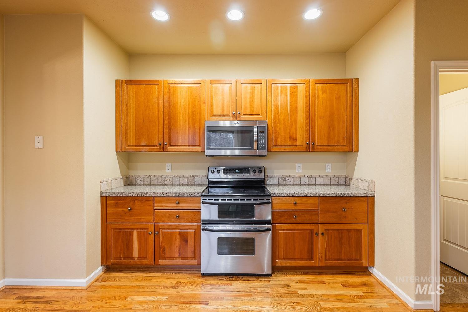 Kitchen with stainless steel appliances, brown cabinets, light wood-style flooring, light stone countertops, and recessed lighting