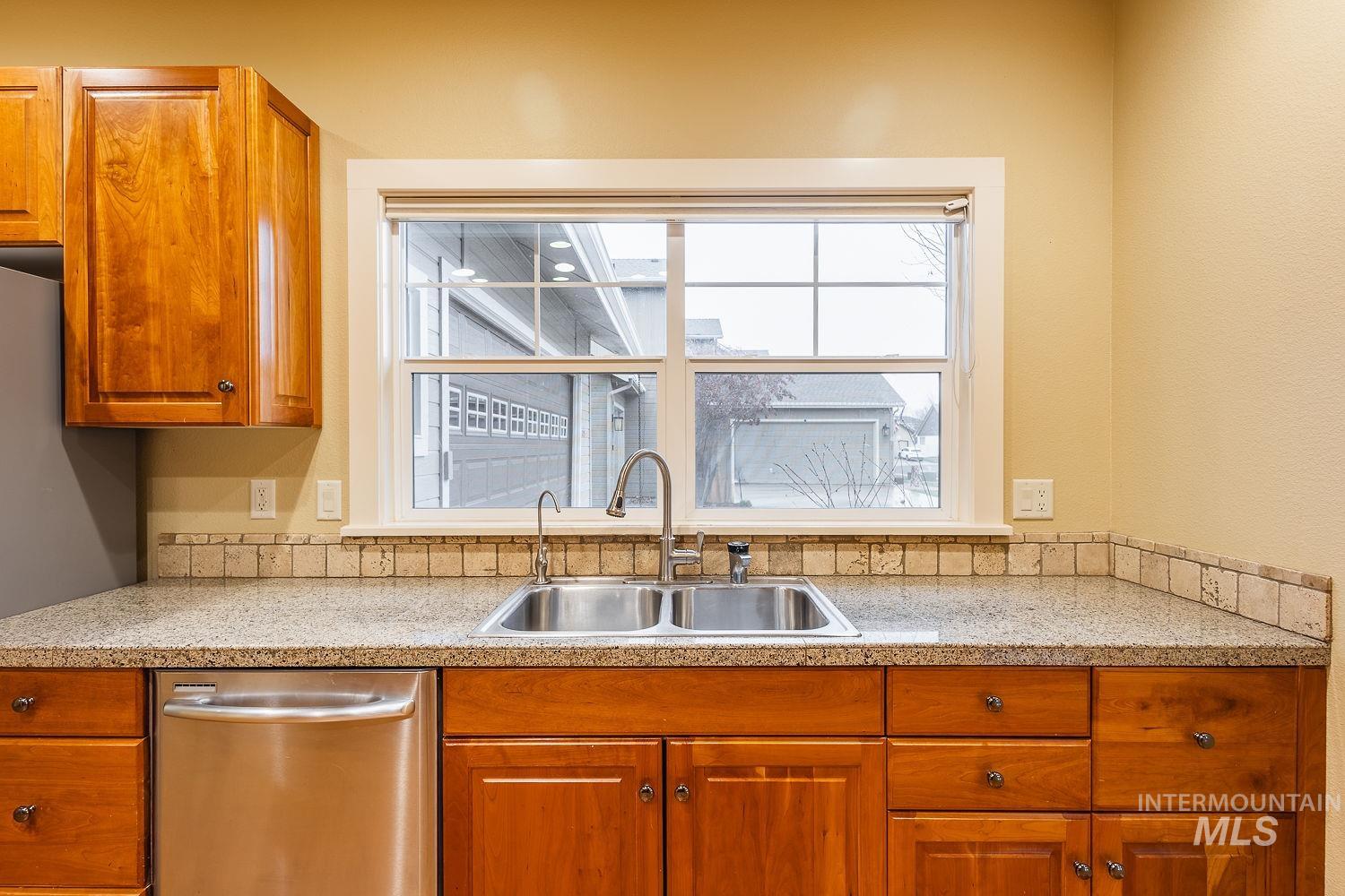 Kitchen with brown cabinets, stainless steel dishwasher, healthy amount of natural light, and light stone counters