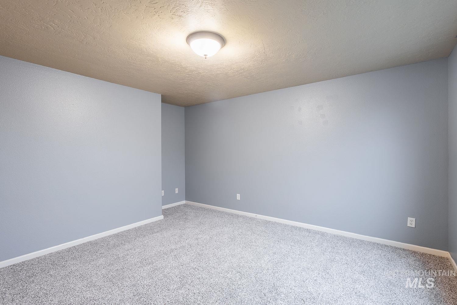 Carpeted empty room with a textured ceiling and baseboards
