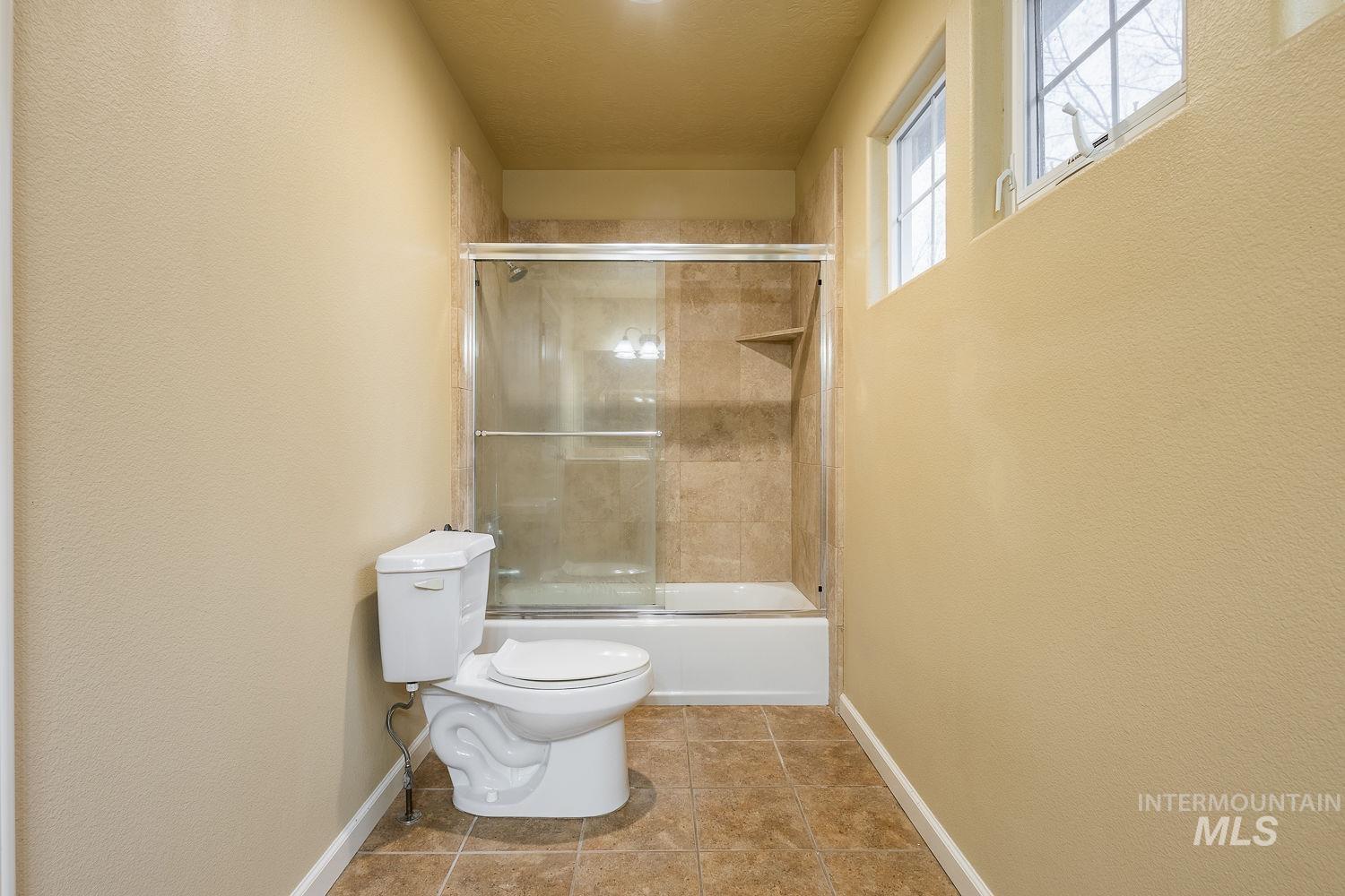 Bathroom with enclosed tub / shower combo, tile patterned floors, and a textured wall