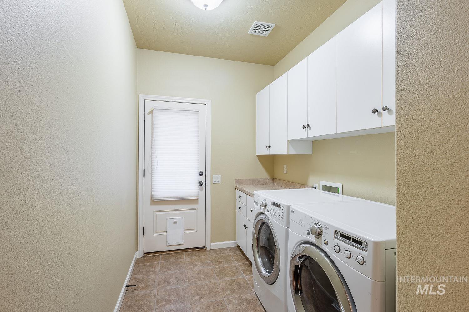 Washroom featuring cabinet space, separate washer and dryer, light tile patterned flooring, and a textured ceiling