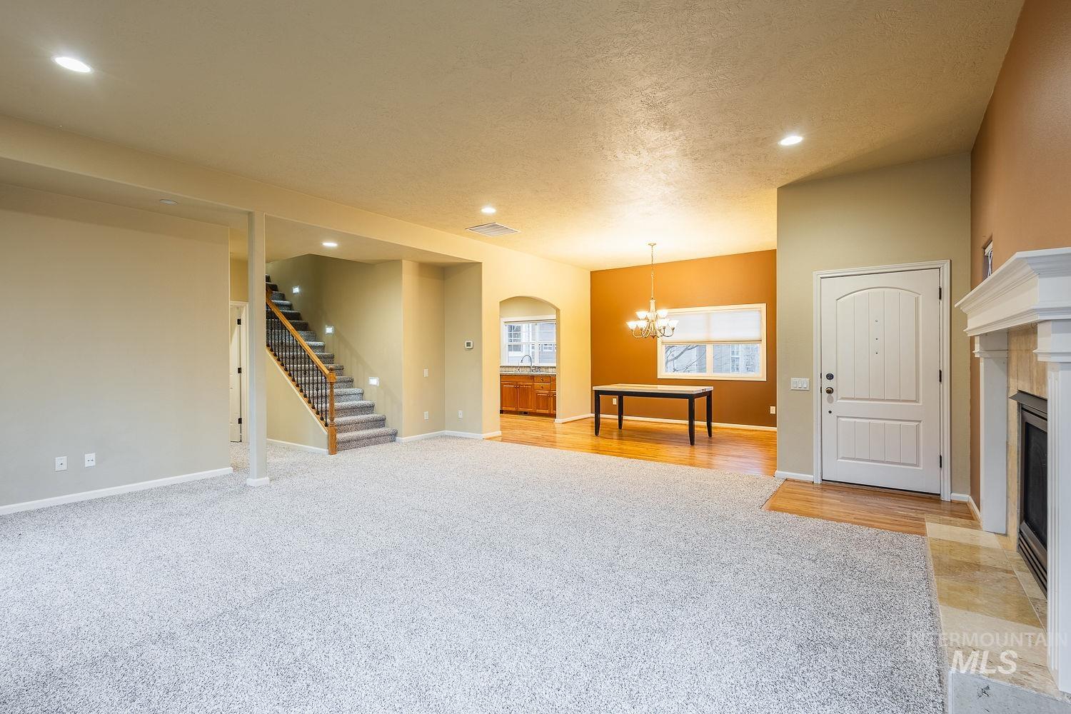 Unfurnished living room featuring light colored carpet, a chandelier, a fireplace with flush hearth, arched walkways, and a textured ceiling