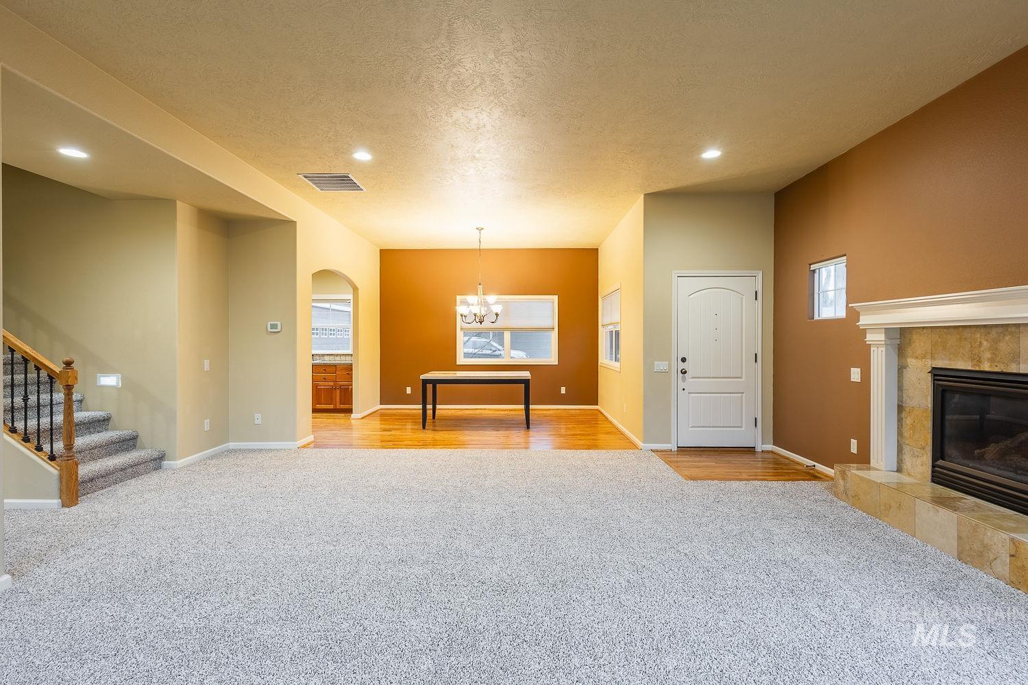 Unfurnished living room featuring light carpet, a fireplace, a textured ceiling, recessed lighting, and stairway