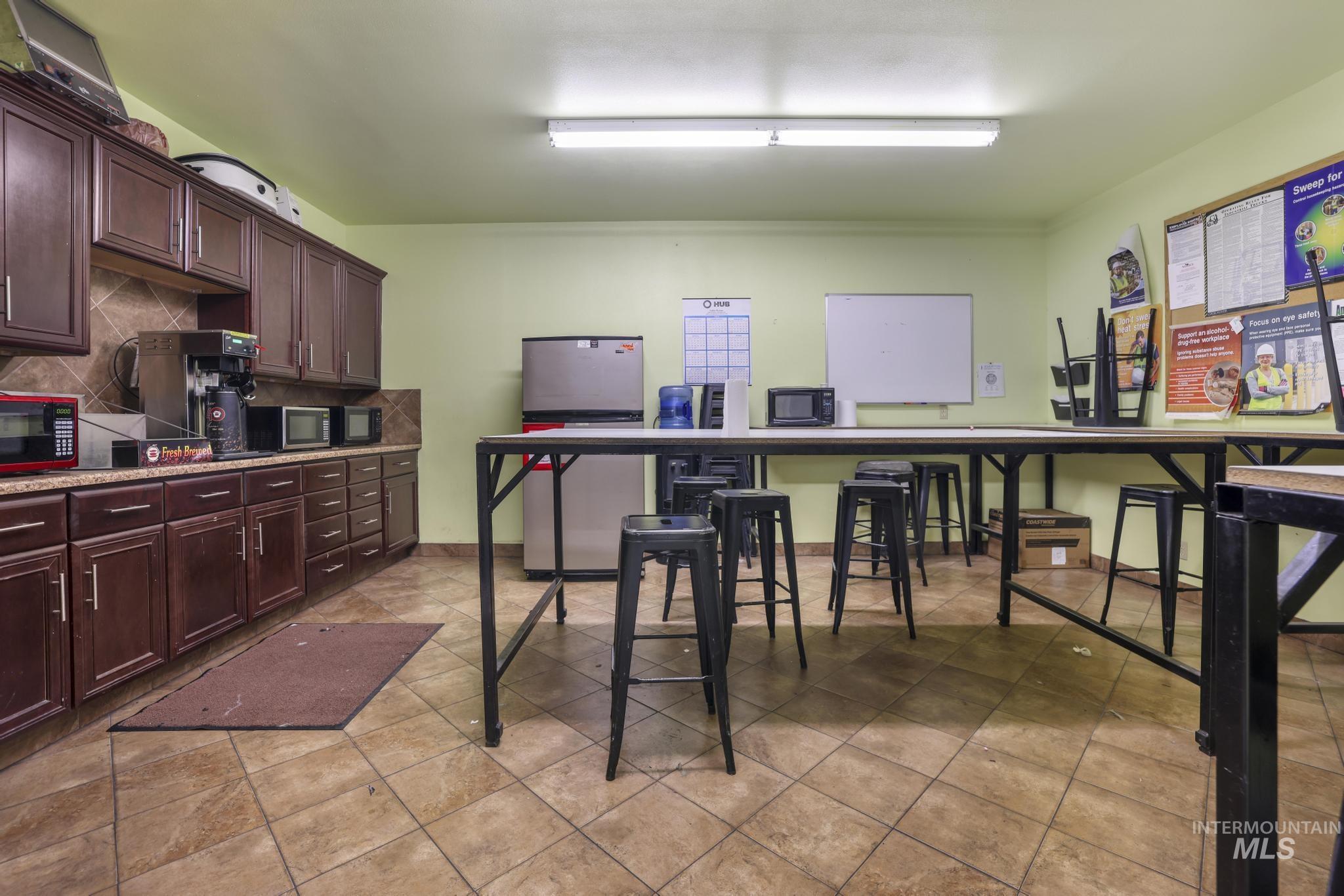 Kitchen with dark brown cabinetry, stainless steel microwave, light stone counters, and black microwave