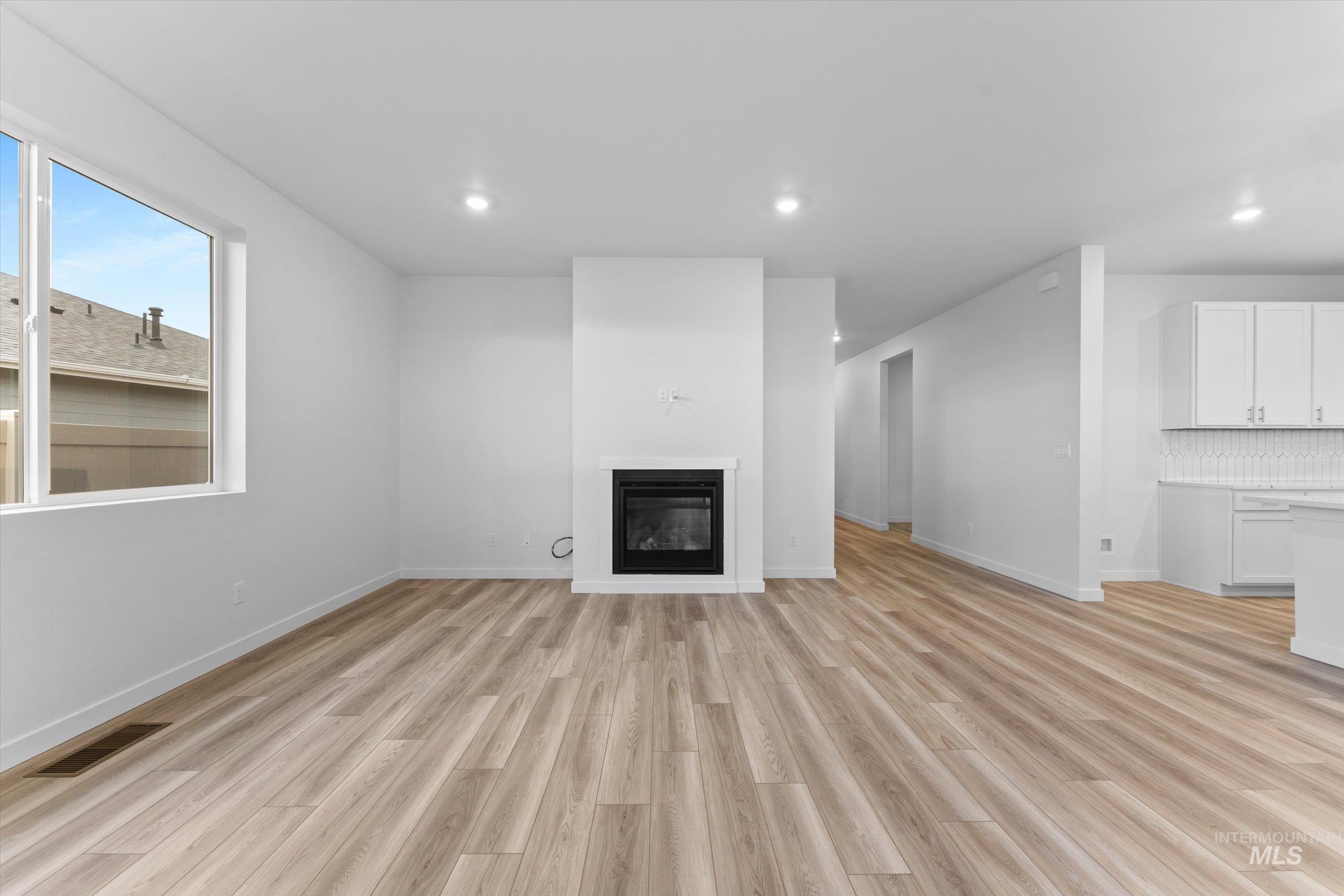 Unfurnished living room featuring light wood finished floors, a glass covered fireplace, and recessed lighting