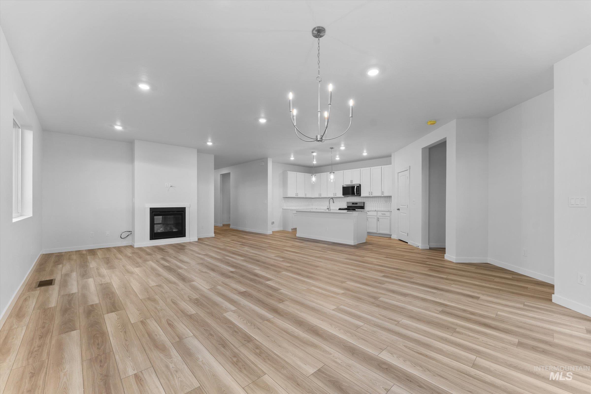 Unfurnished living room with a chandelier, light wood finished floors, recessed lighting, and a glass covered fireplace