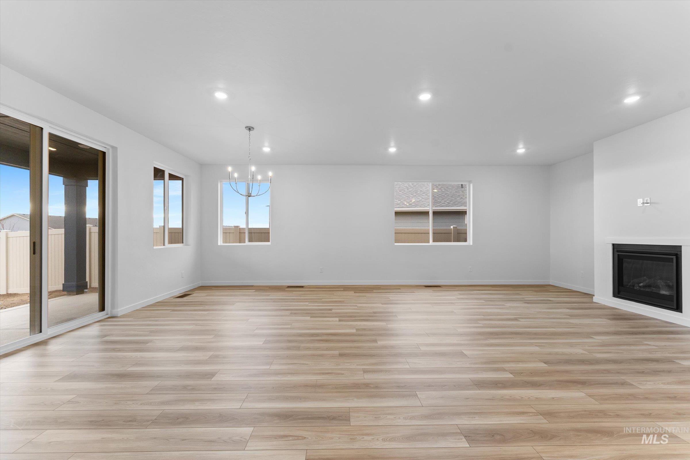 Unfurnished living room featuring recessed lighting, light wood-style floors, a glass covered fireplace, and a chandelier