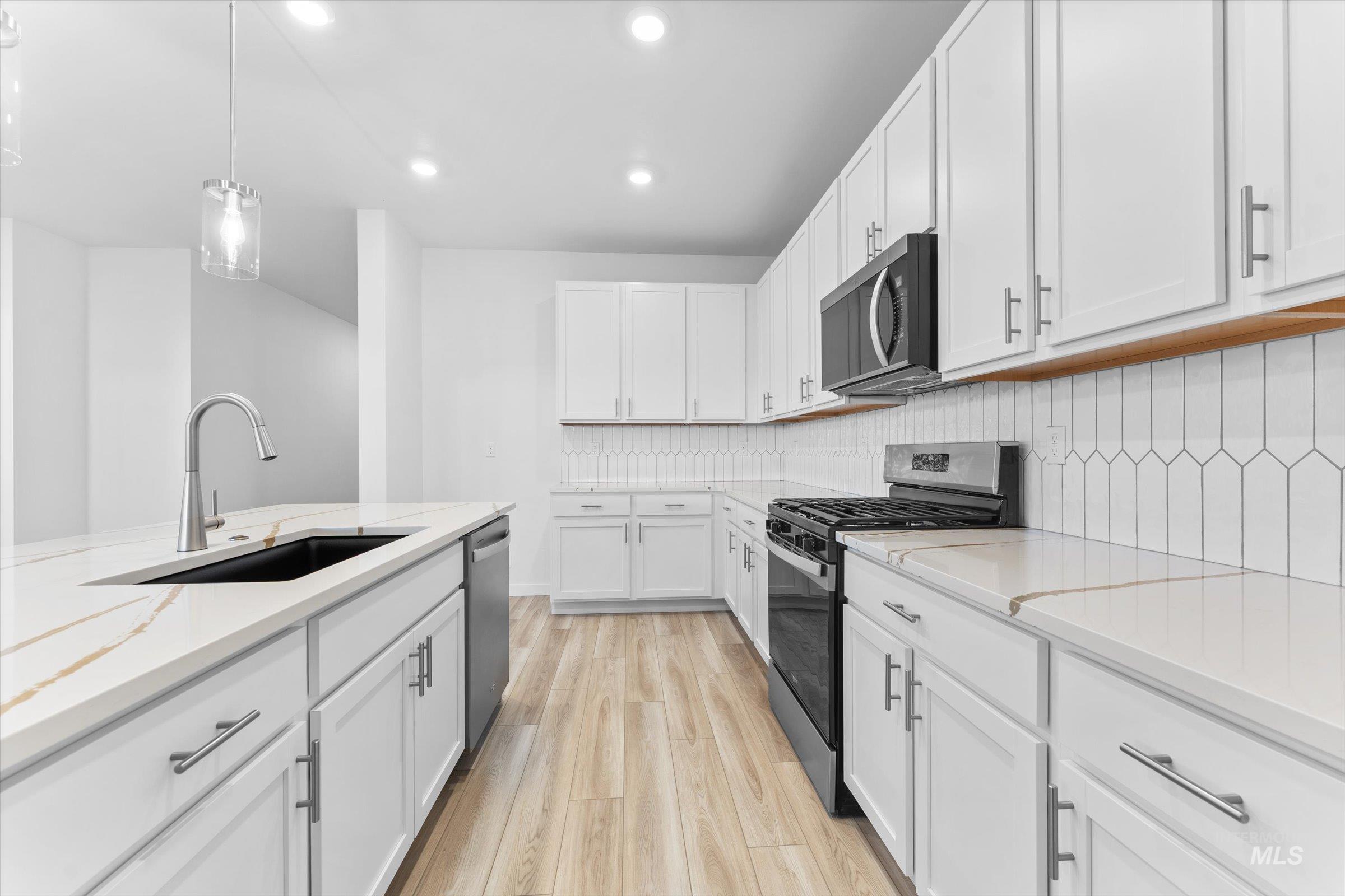 Kitchen featuring stainless steel appliances, white cabinetry, hanging light fixtures, light wood-style floors, and backsplash