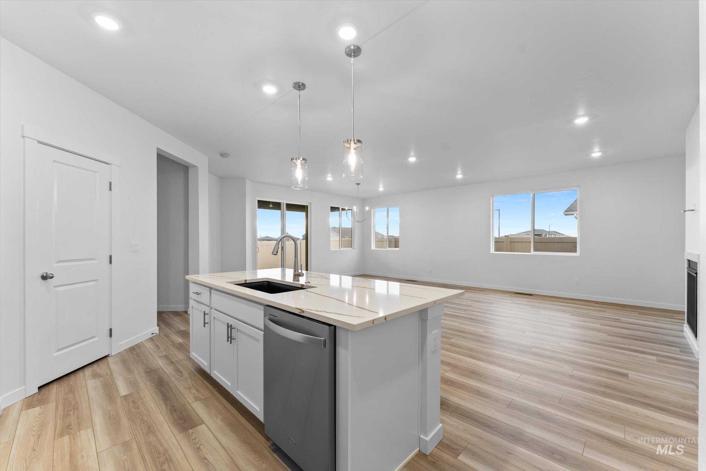 Kitchen featuring stainless steel dishwasher, white cabinetry, decorative light fixtures, an island with sink, and light wood finished floors
