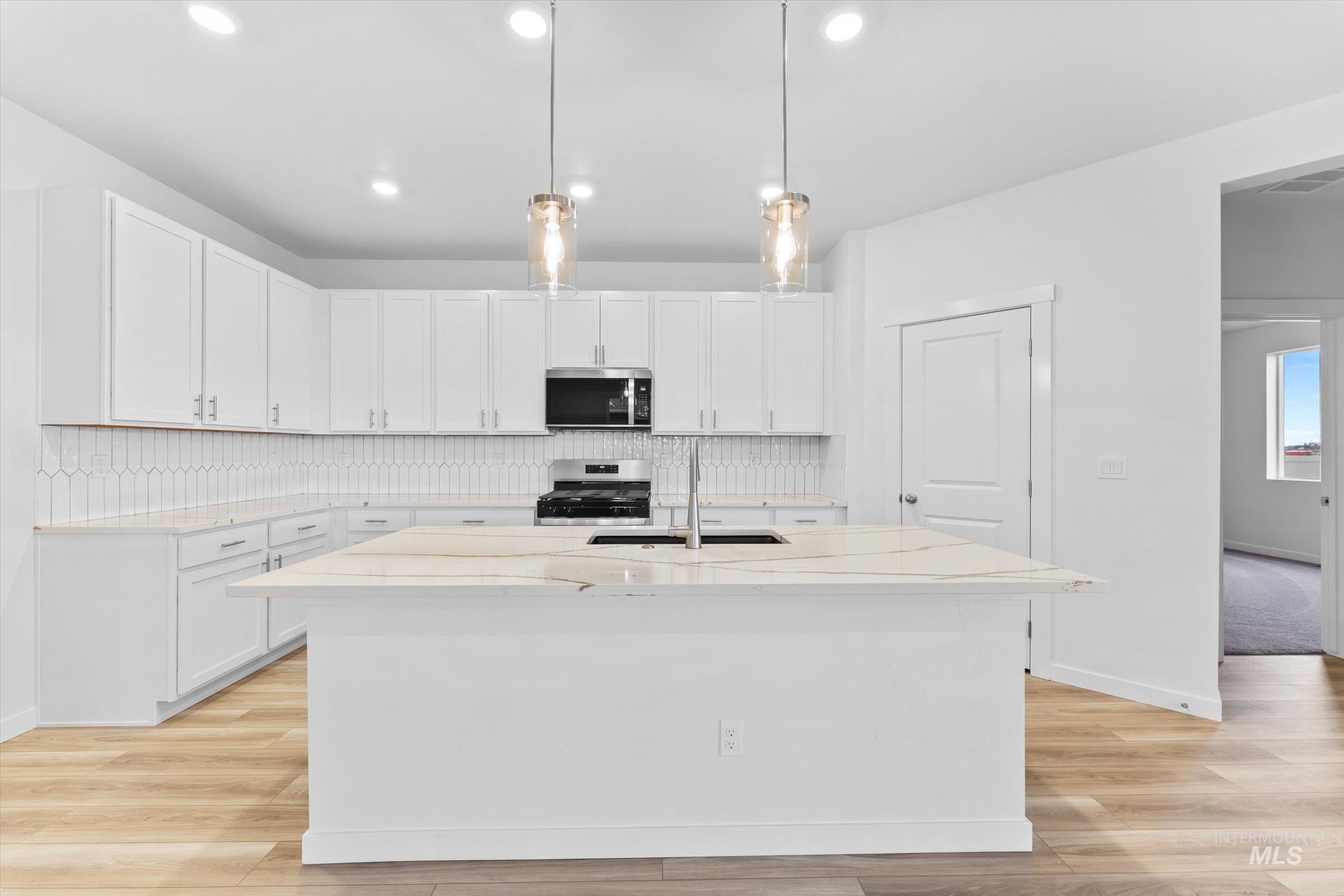 Kitchen featuring pendant lighting, tasteful backsplash, light stone countertops, white cabinets, and recessed lighting
