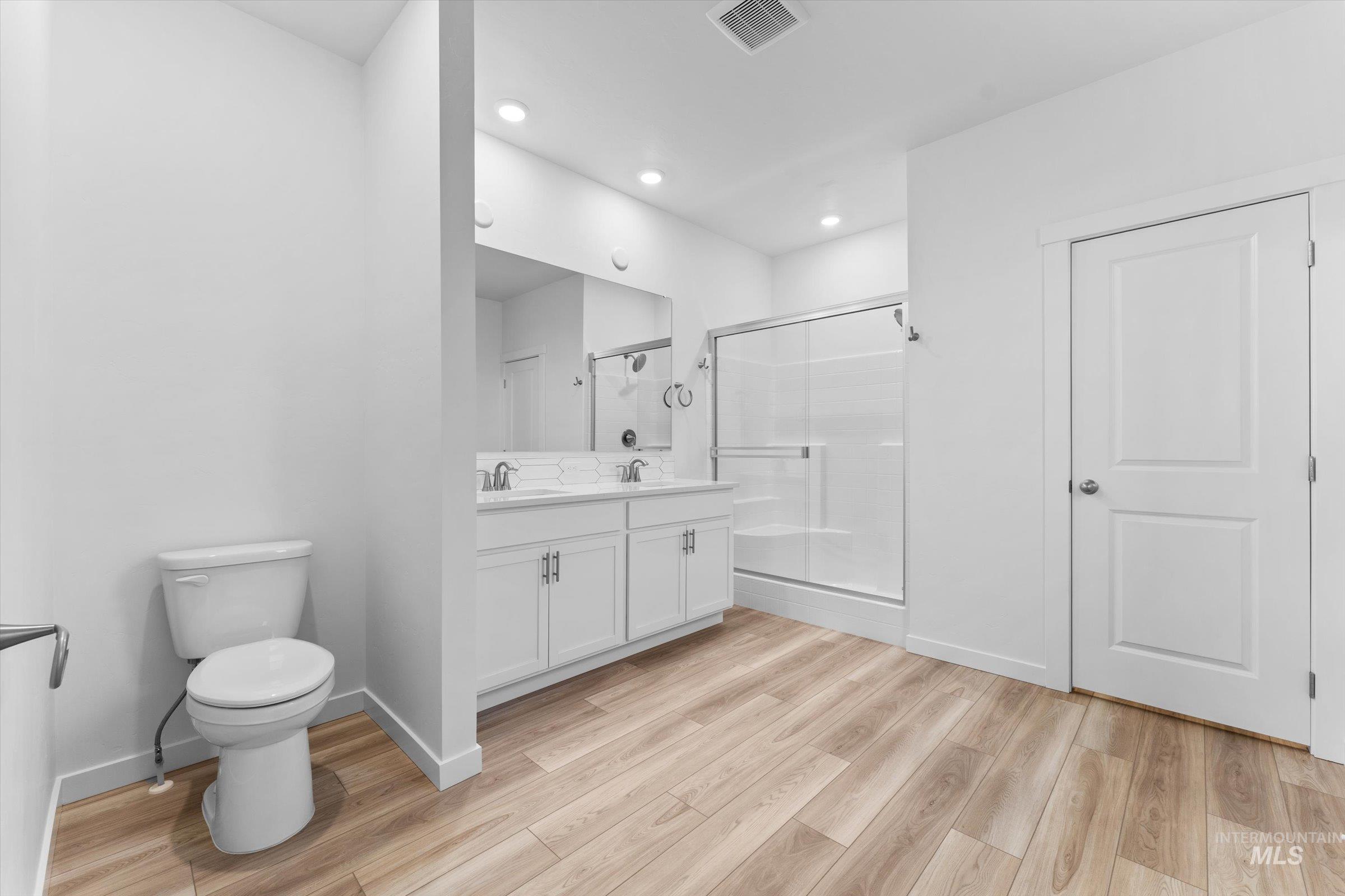 Full bath with double vanity, a stall shower, light wood-type flooring, and recessed lighting