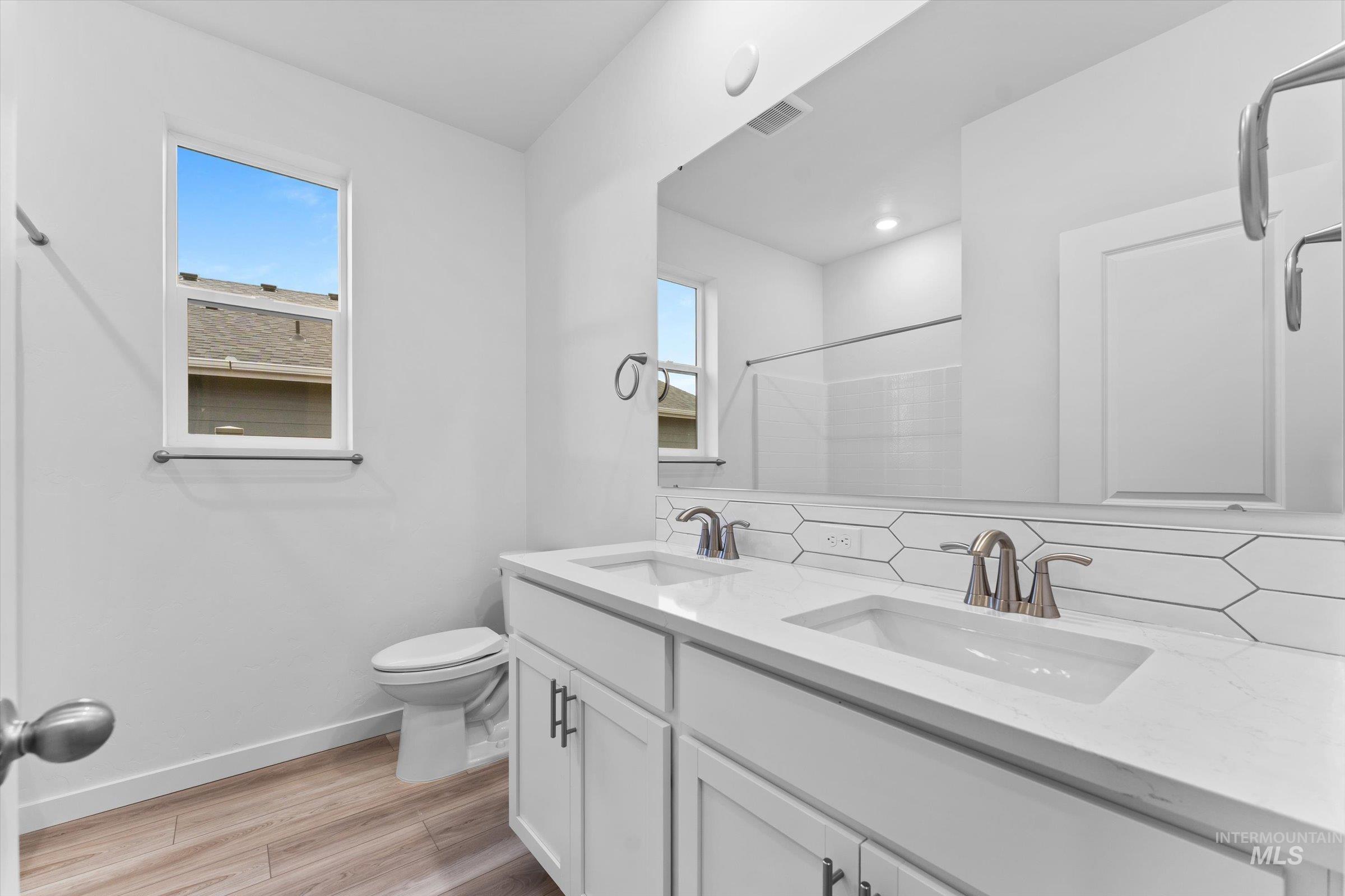 Full bathroom with double vanity, light wood-style flooring, tasteful backsplash, a shower, and plenty of natural light