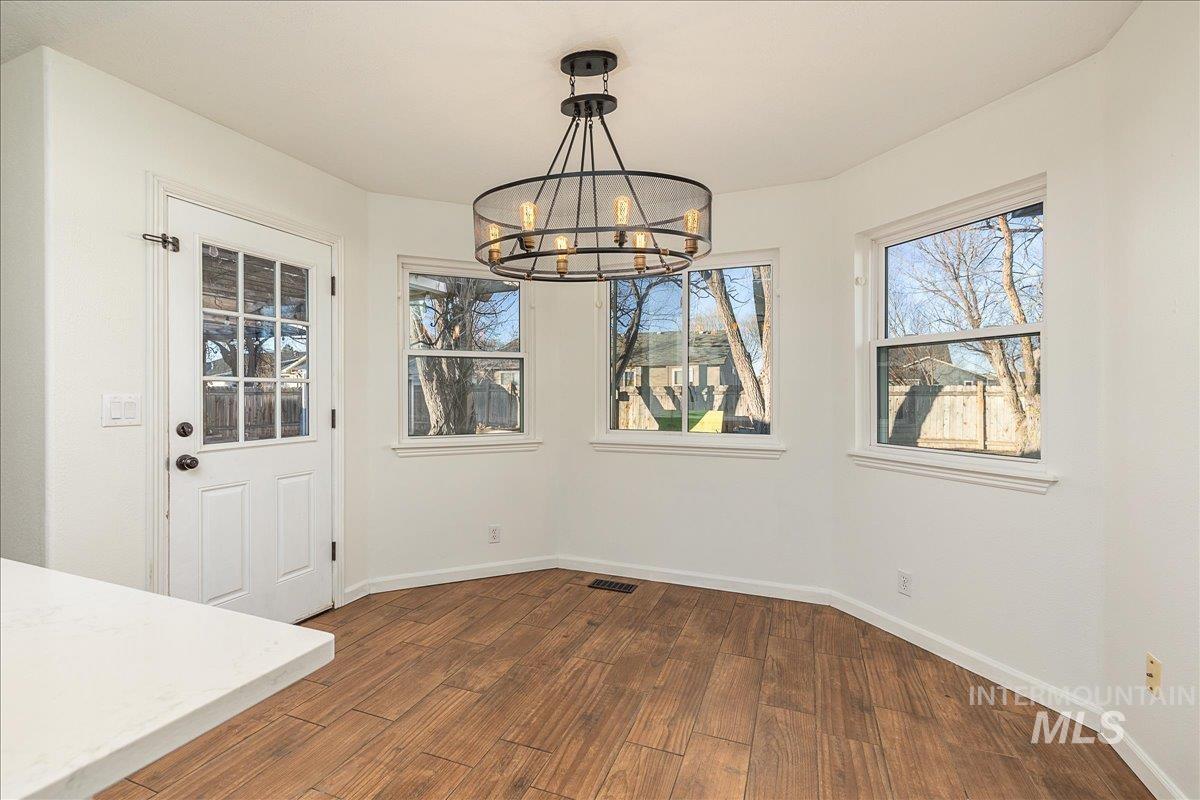 Unfurnished dining area featuring dark wood-type flooring, healthy amount of natural light, and a chandelier