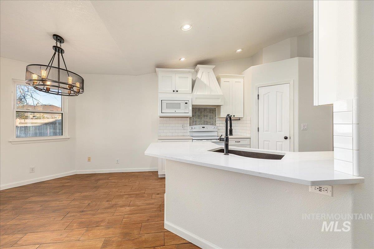 Kitchen with white cabinets, custom exhaust hood, light stone countertops, decorative backsplash, and a peninsula