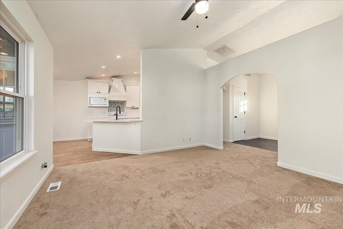 Unfurnished living room with vaulted ceiling, light carpet, a ceiling fan, arched walkways, and recessed lighting