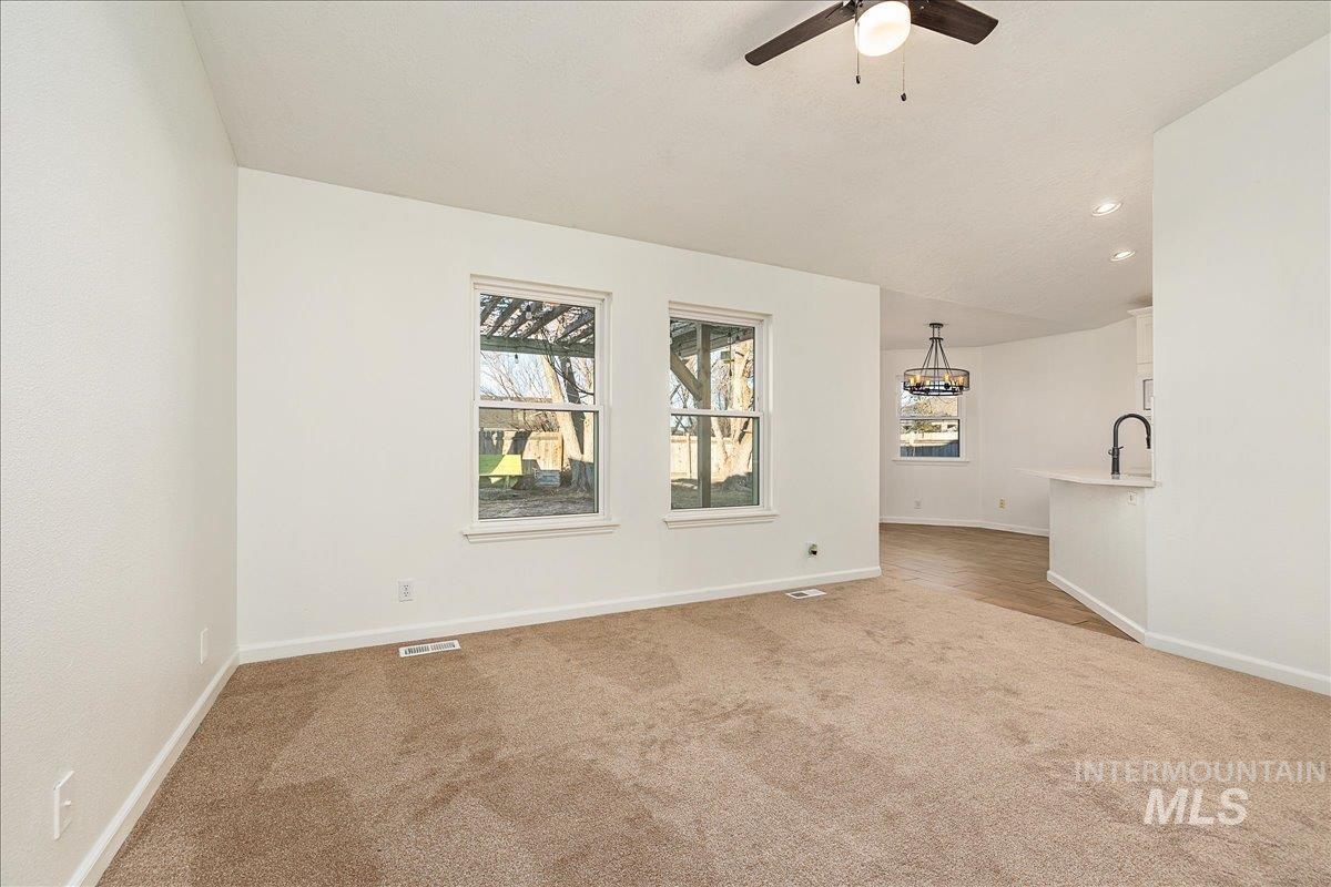 Empty room featuring light colored carpet, lofted ceiling, recessed lighting, a chandelier, and a ceiling fan